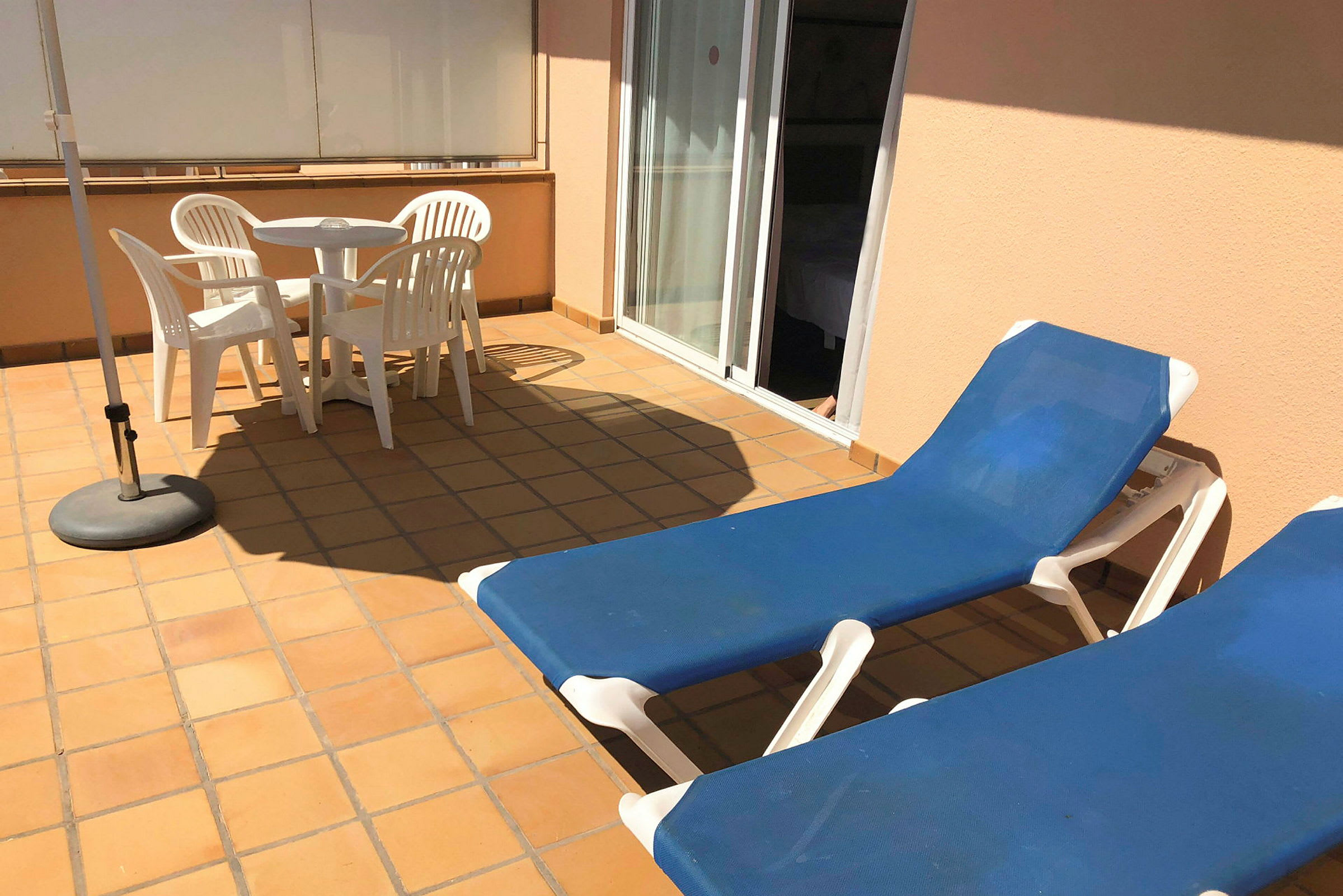 Terrasse med to liggestole, et hvidt bord og fire hvide stole samt en parasol. (AI-genereret tekst)