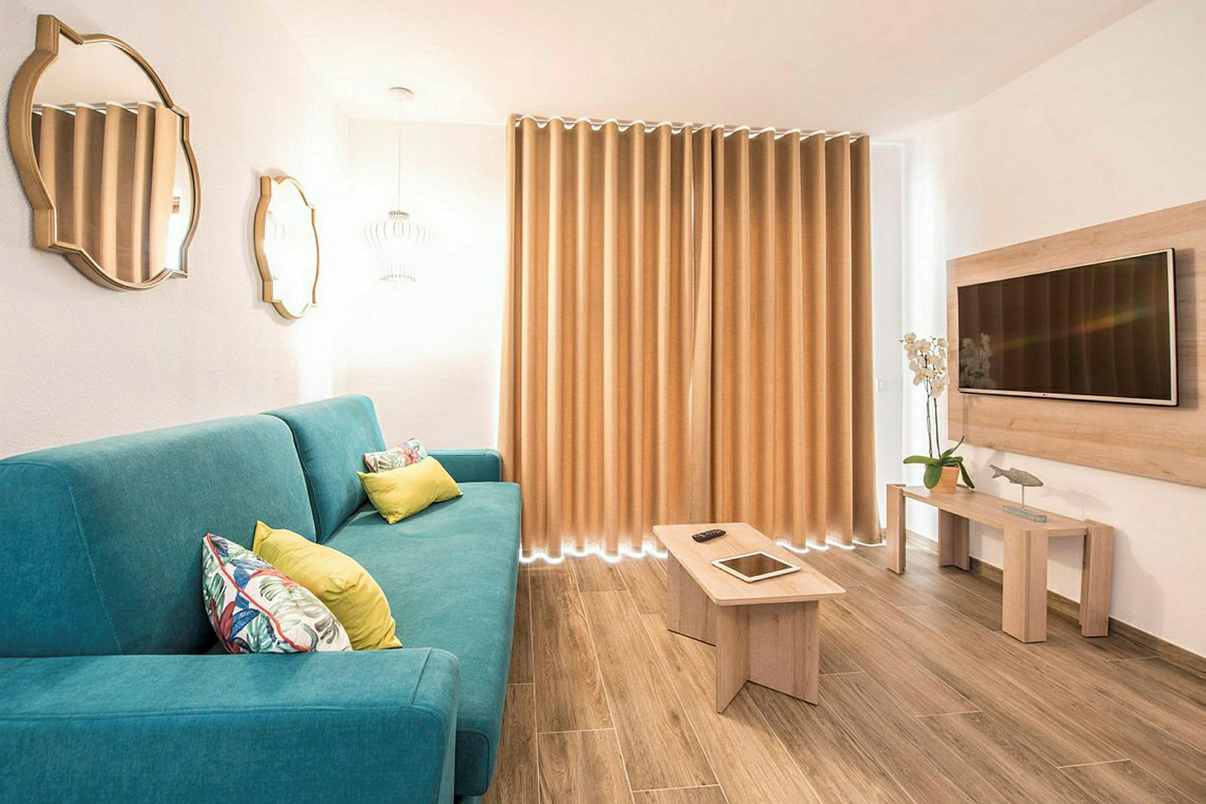 En moderne stue med en blå sofa, træbord, vægmonteret TV og gardiner. (AI-genereret tekst)