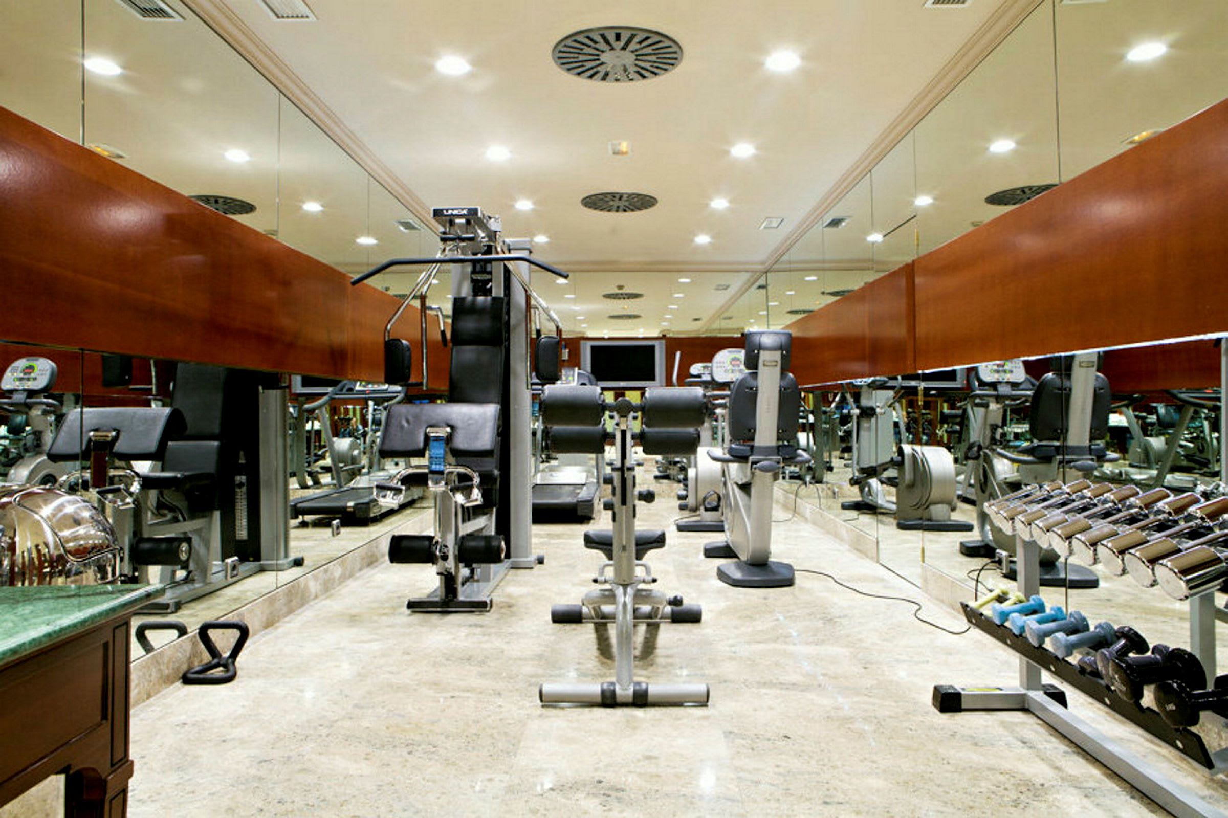 Et fitnesscenter med træningsmaskiner og frie vægte, spejle dækker væggene. (AI-genereret tekst)