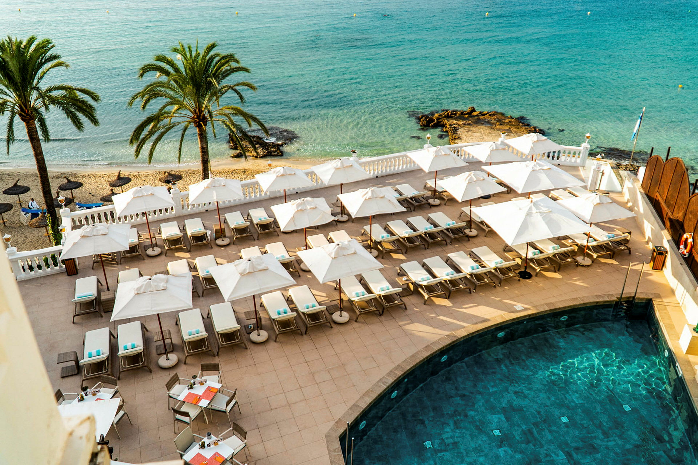 Liggestole og parasoller på en terrasse ved siden af en pool med udsigt over stranden og havet. (AI-genereret tekst)