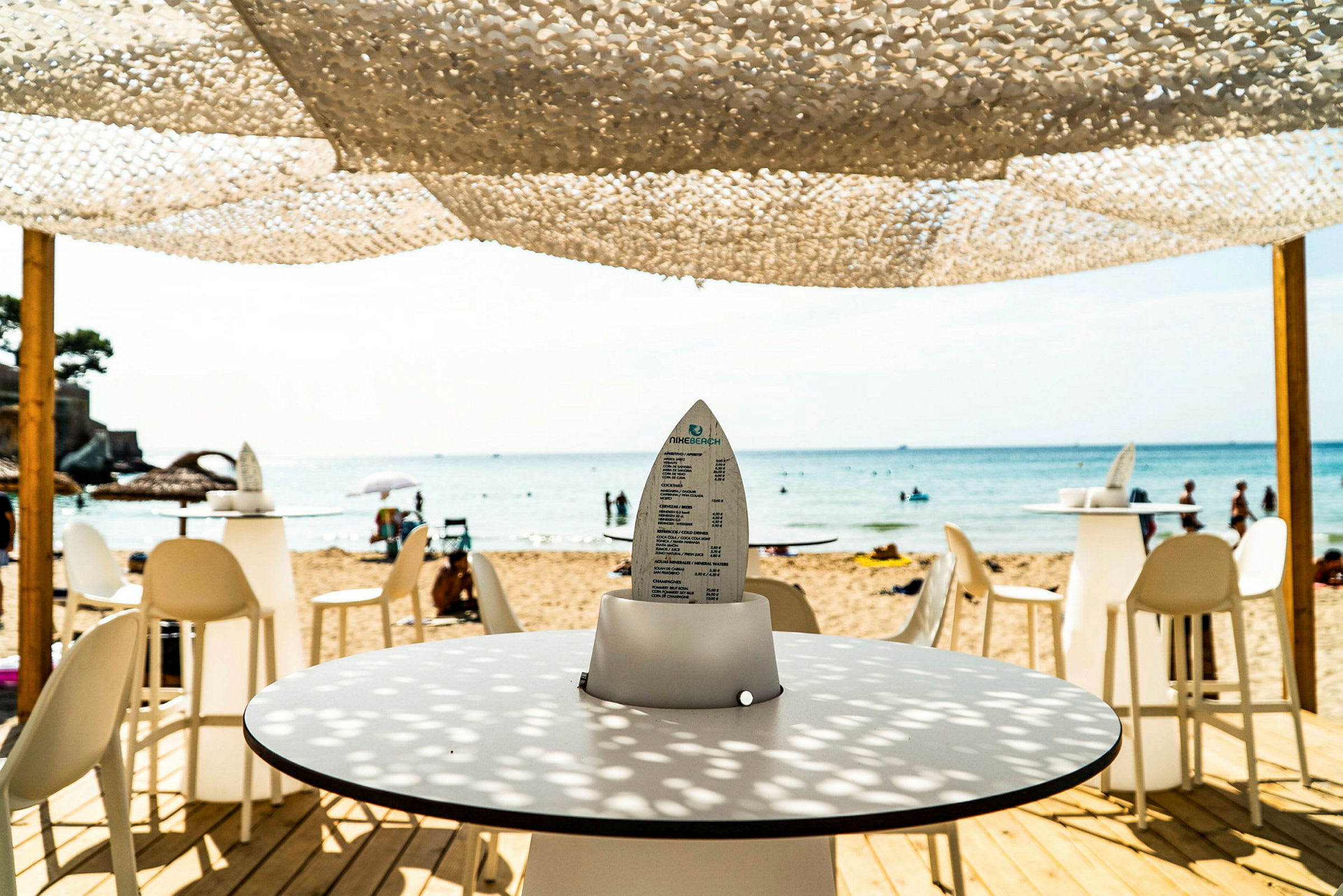Udsigt fra en strandbar mod havet med borde og stole. (AI-genereret tekst)