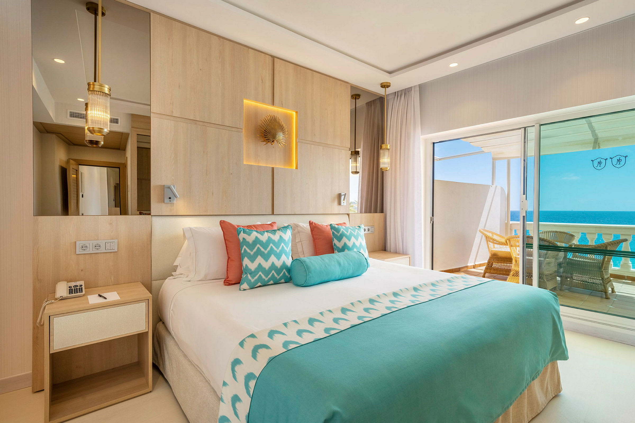 Hotelværelse med dobbeltseng, dekoreret i blåt og hvidt, med udsigt over havet fra en balkon. (AI-genereret tekst)
