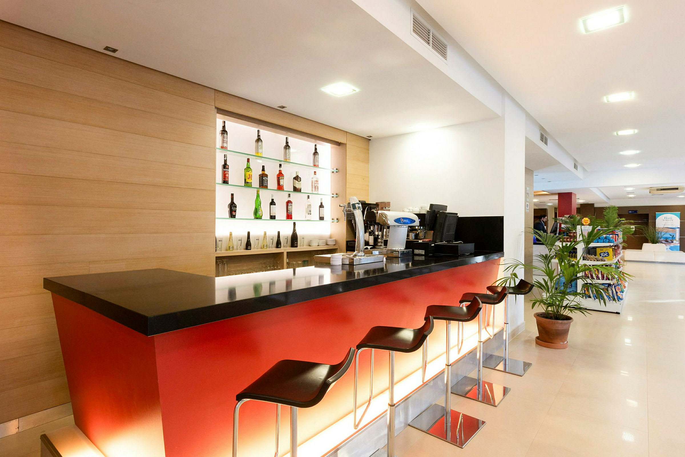 En moderne hotelbar med røde paneler, sort bordplade og flere barstole. (AI-genereret tekst)