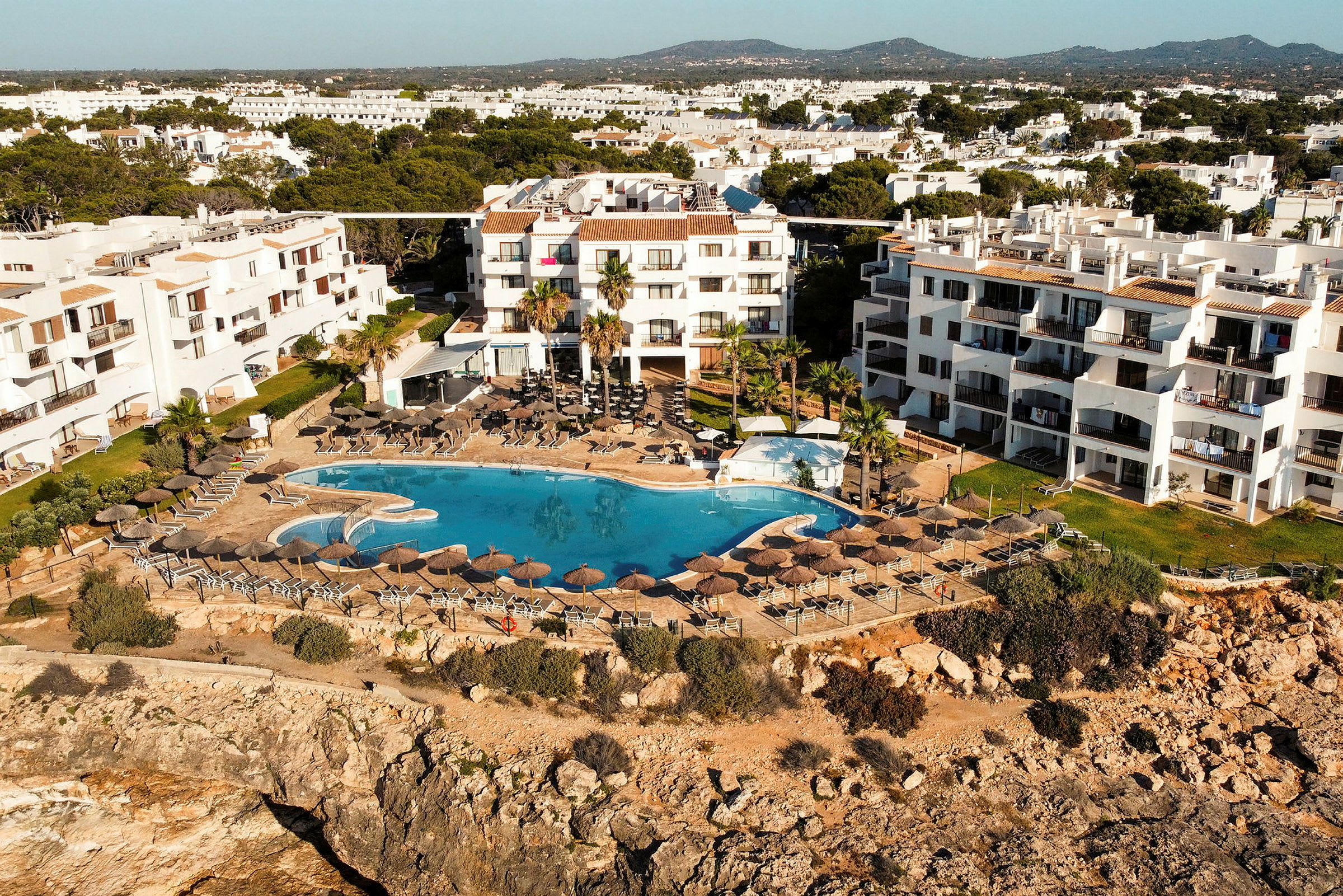 Hotel med hvid facade ved klippekant med pool og solsenge. (AI-genereret tekst)