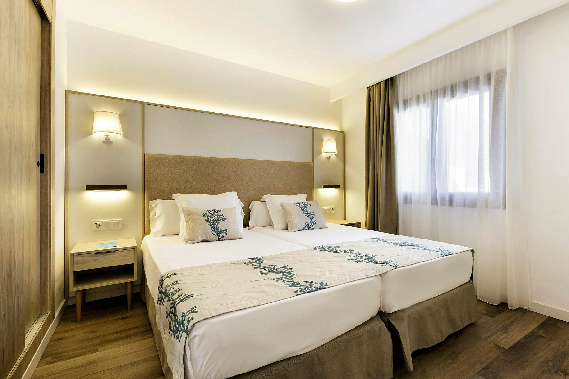 Moderne indrettet hotelværelse med en dobbeltseng, natbord og et vindue med lyse gardiner. (AI-genereret tekst)