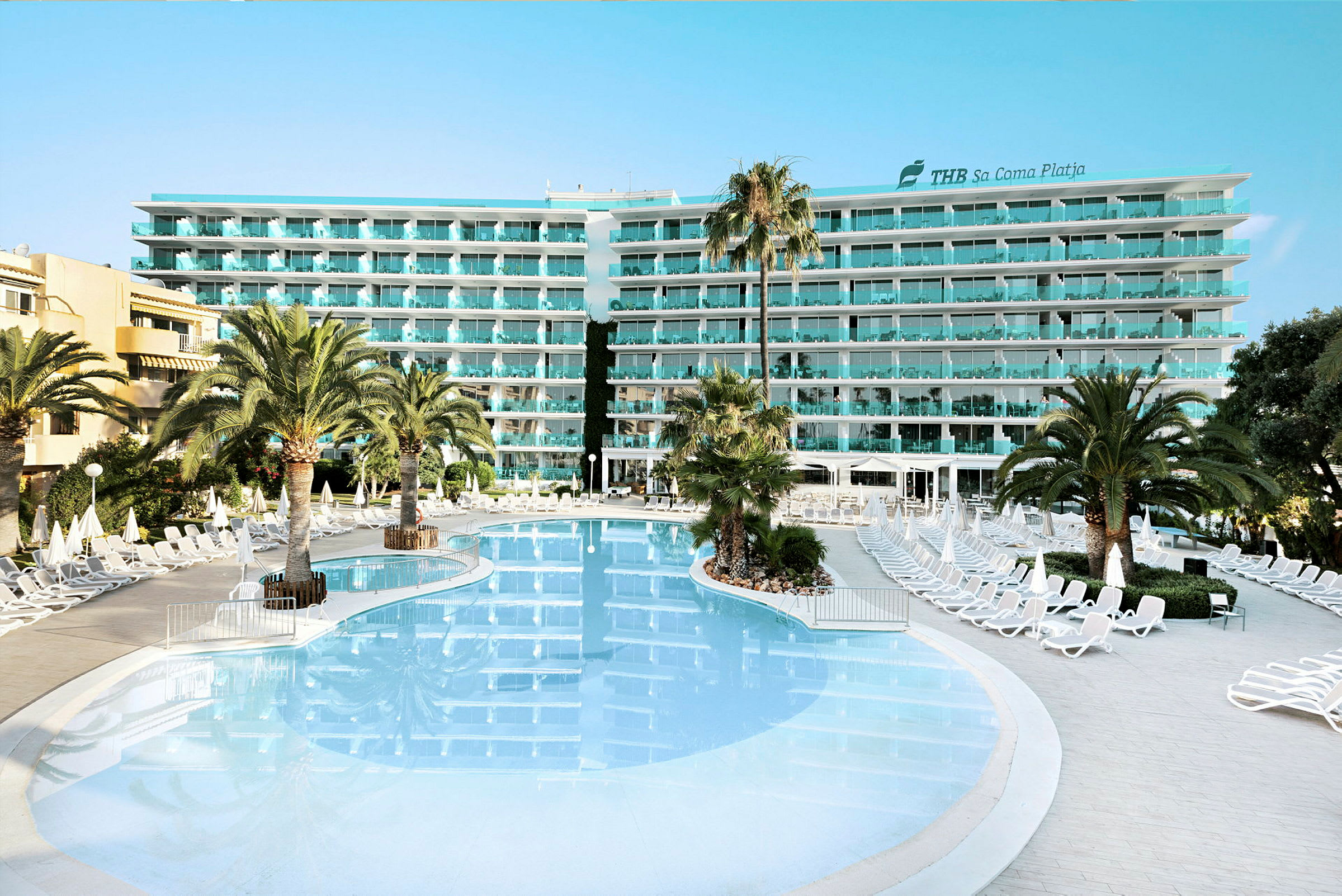 Hotelbygning med flere etager set bag en stor pool og liggestole. (AI-genereret tekst)