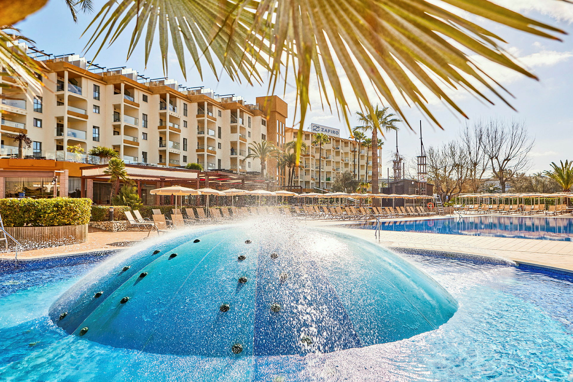 Hotellets poolområde med liggestole og en fontæne. (AI-genereret tekst)
