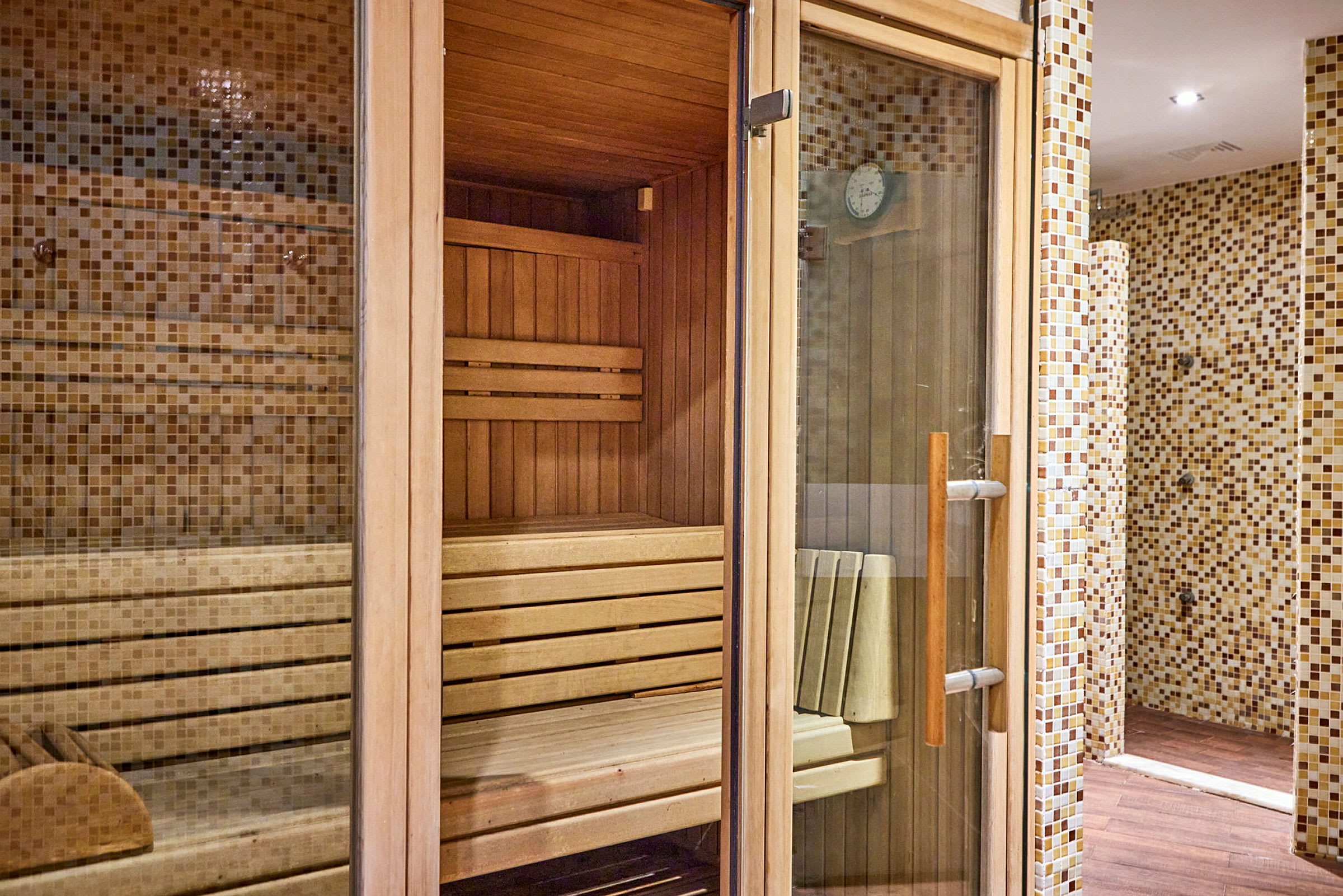 En træbeklædt sauna med glaspaneler og flisebelagte vægge udenfor. (AI-genereret tekst)