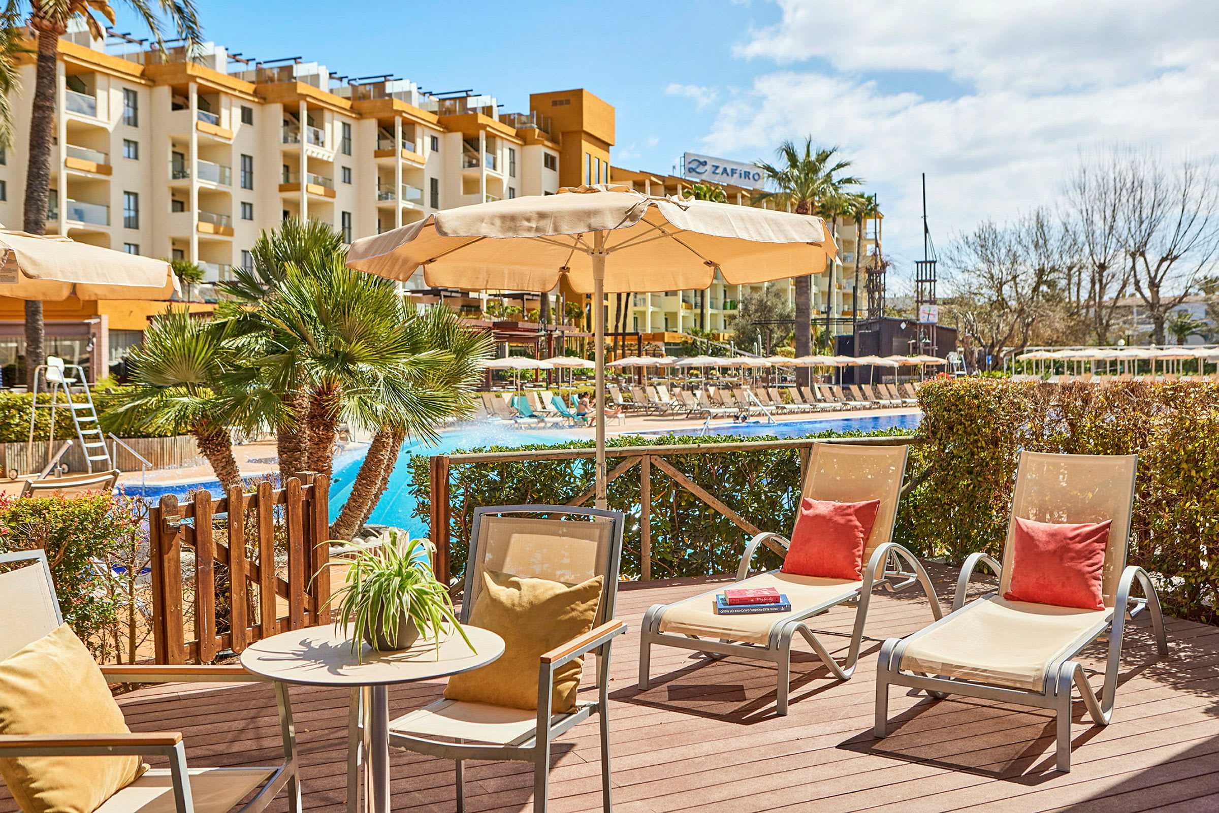 Udendørsområde ved pool med liggestole og parasoller, hotelbygning i baggrunden. (AI-genereret tekst)