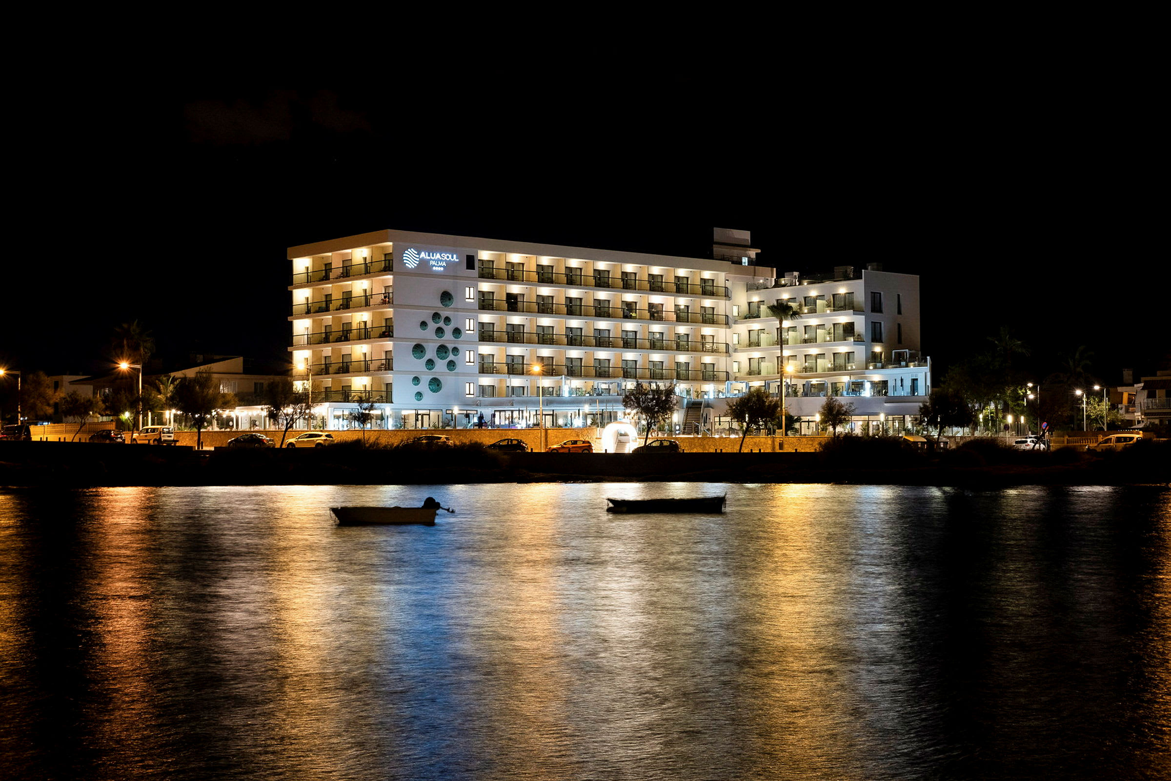 Hotelbygning med oplyste altaner ved vandet om aftenen. (AI-genereret tekst)