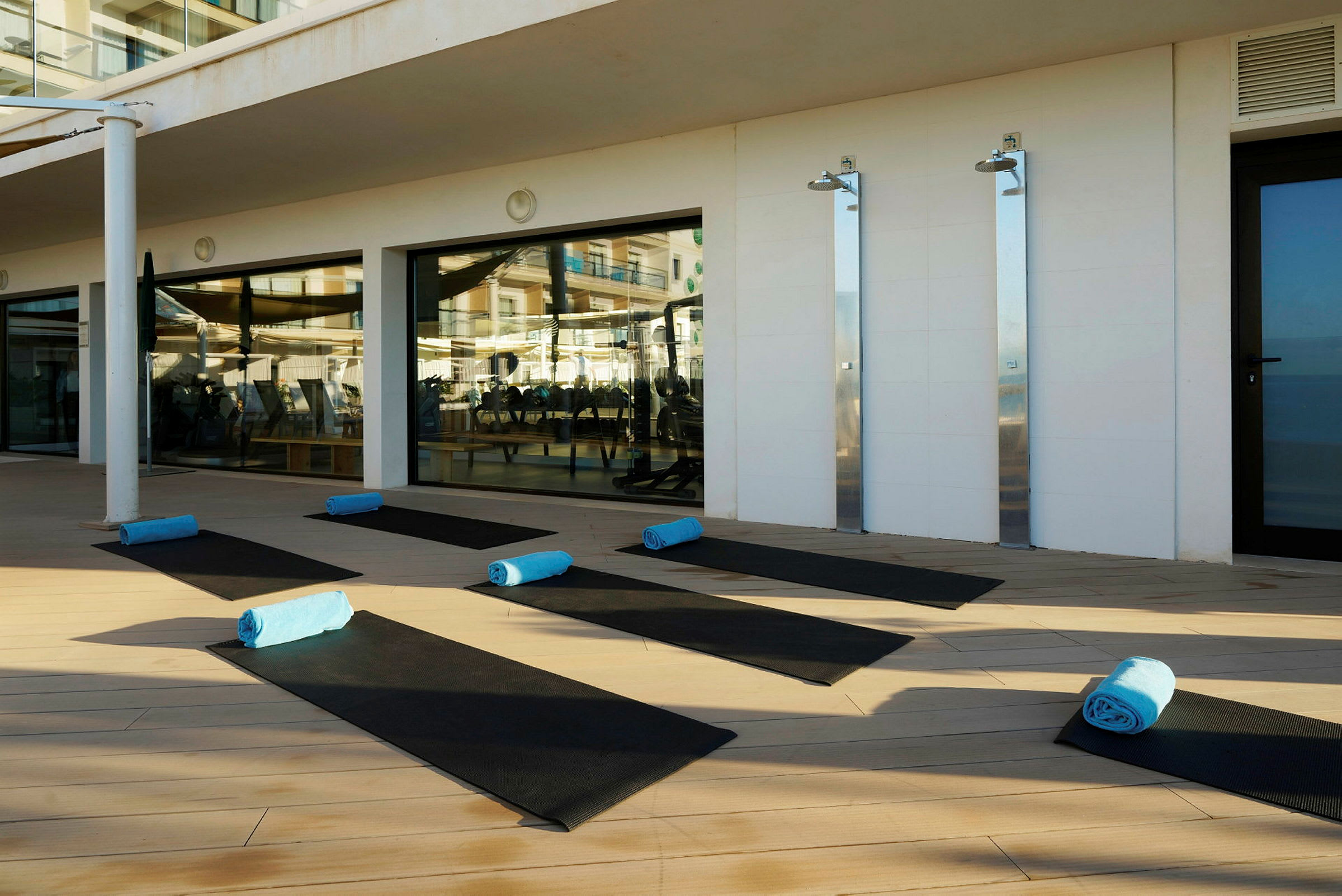 Sorte yogamåtter med blå håndklæder placeret på et trægulv ved siden af et fitnessområde. (AI-genereret tekst)
