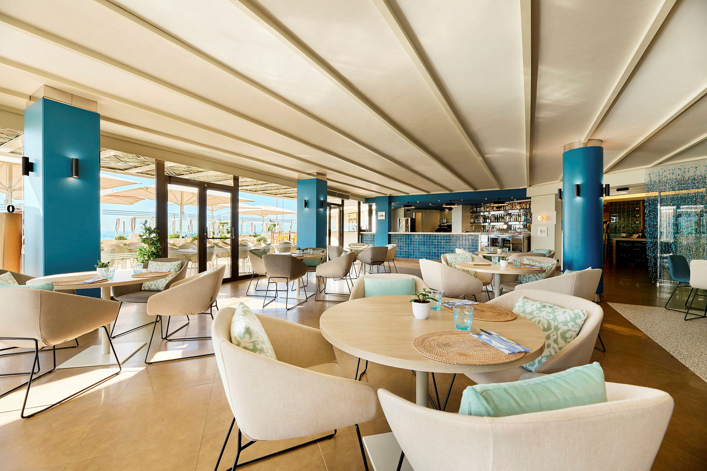 En moderne restaurant med borde og stole, indrettet i lyse farver og med udsigt til en terrasse. (AI-genereret tekst)