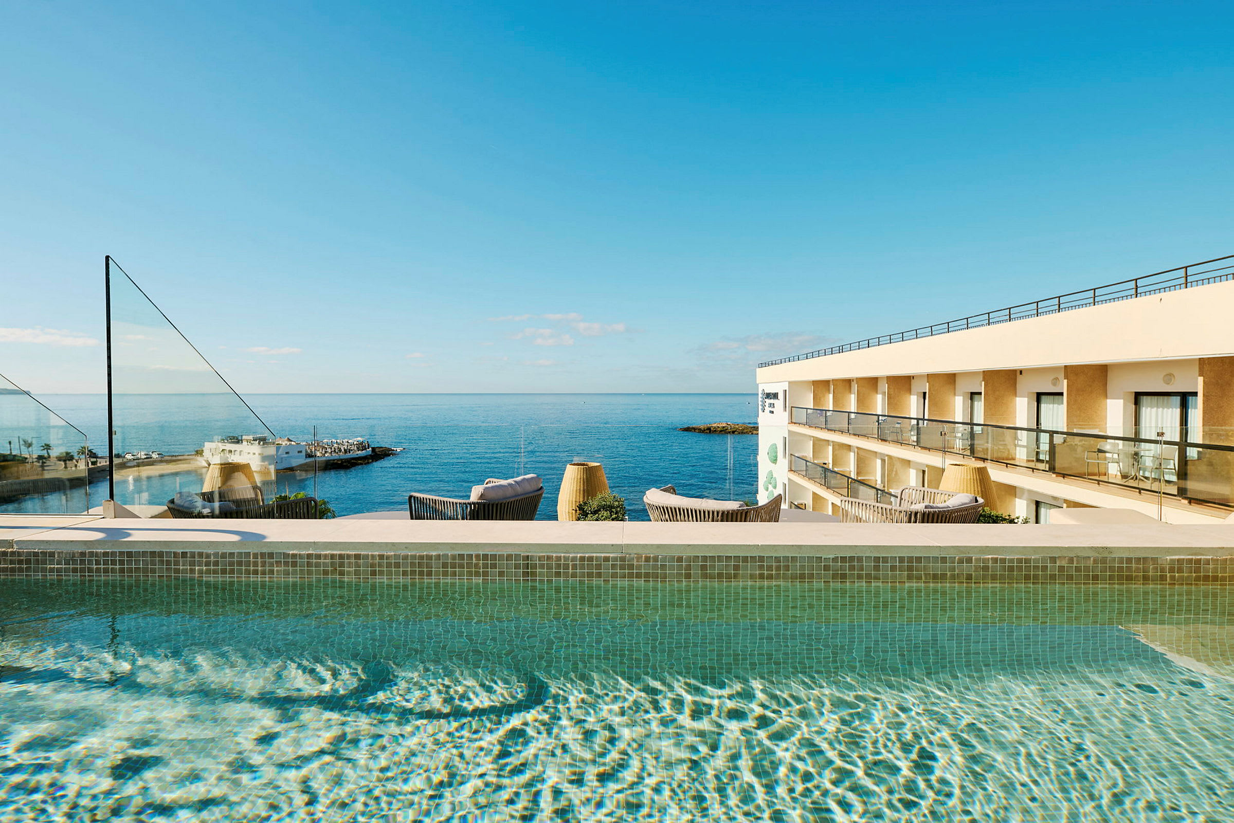 Udendørs pool med udsigt over havet og en hotelbygning. (AI-genereret tekst)