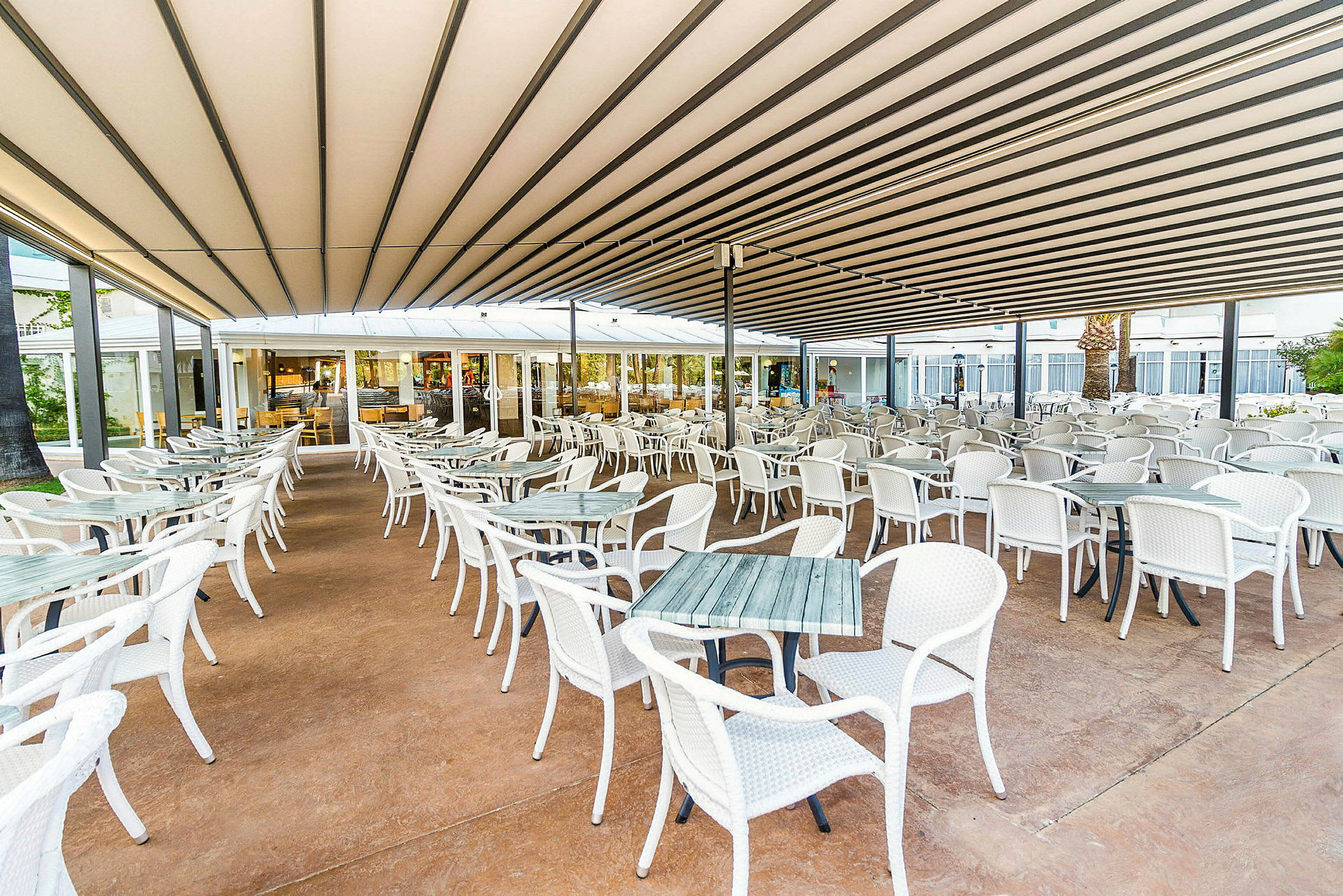En udendørs restaurant med mange hvide borde og stole under et tag. (AI-genereret tekst)