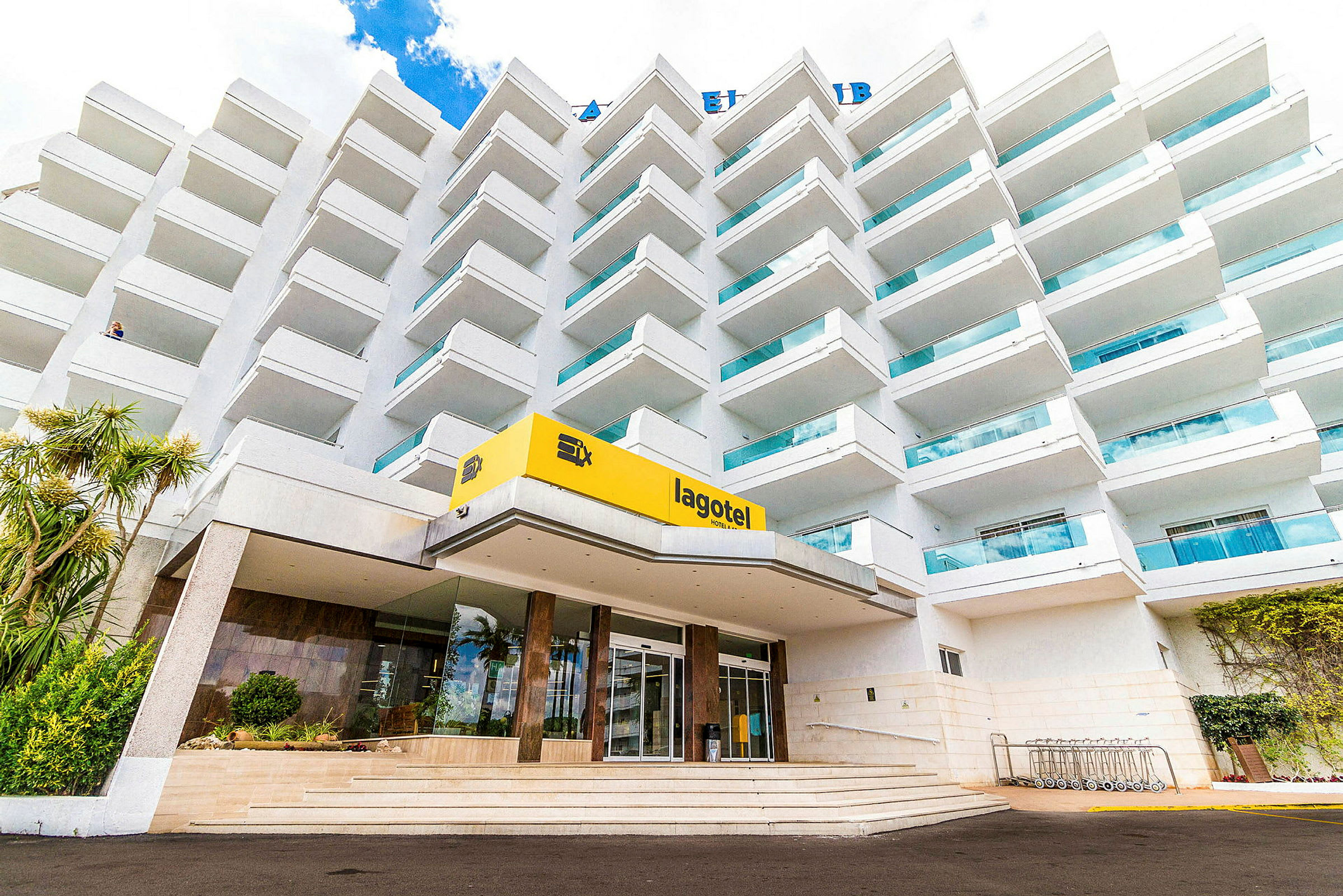 Et fleretagers hotel med altaner og en indgang markeret med et gult skilt, hvorpå der står 'lagotel'. (AI-genereret tekst)