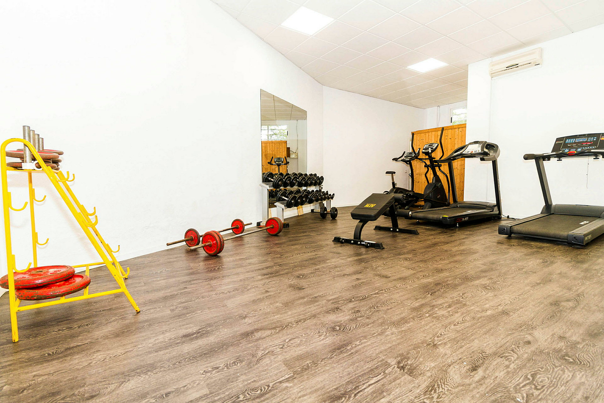 Fitnessrum med træningsudstyr som løbebånd, vægte og en træningsbænk. (AI-genereret tekst)