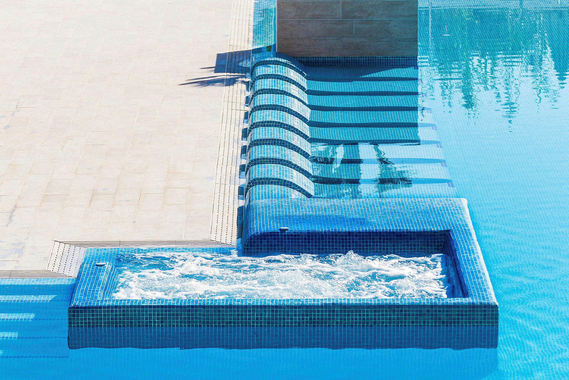 En swimmingpool med blå mosaikfliser og en separat boblebad. (AI-genereret tekst)