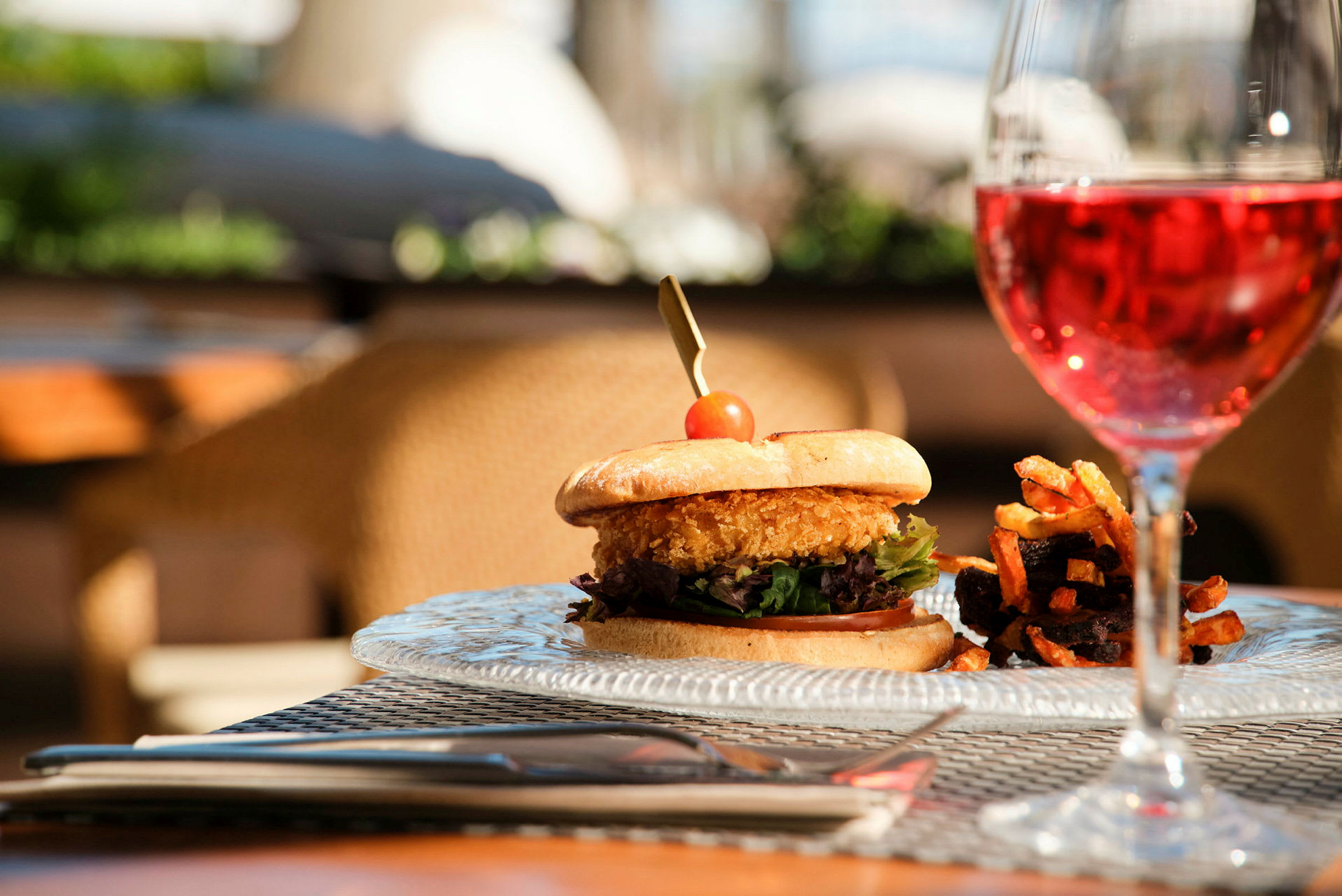 En tallerken med en burger ved siden af pommes frites og et glas rosévin. (AI-genereret tekst)