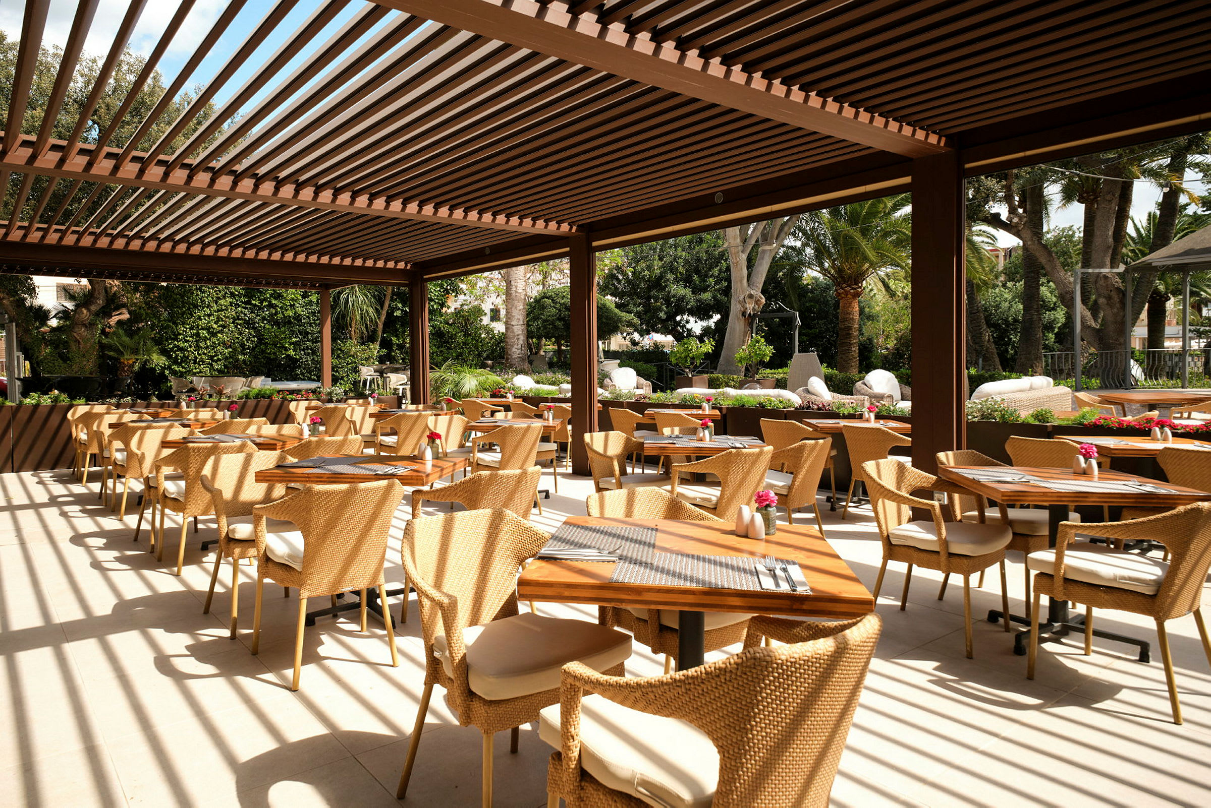 En udendørsrestaurant med borde og stole og pergola. (AI-genereret tekst)