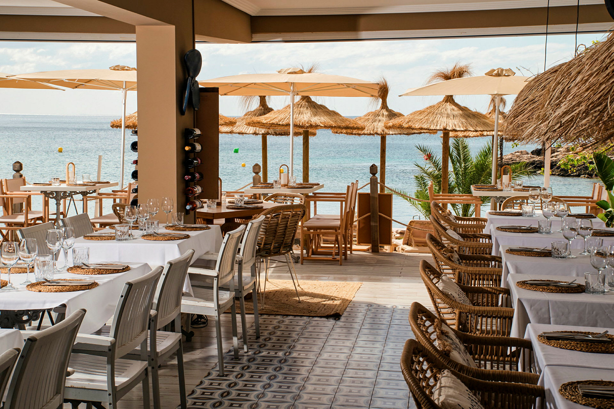 Billede af en restaurant med dækkede borde og udsigt over havet, parasoller og strandfront. (AI-genereret tekst)