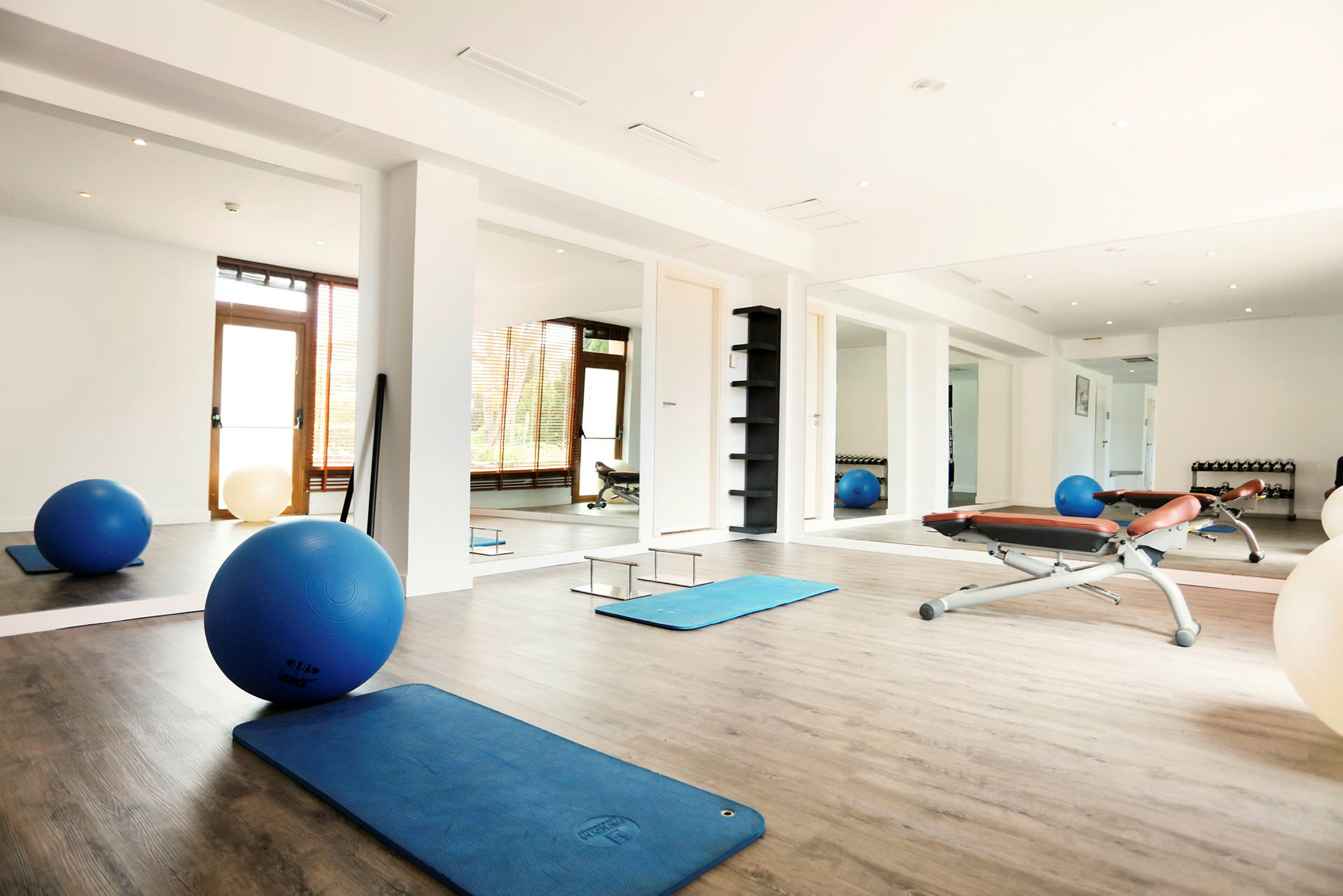 Et lyst fitnessrum med træningsmåtter, pilatesbolde og bænke. (AI-genereret tekst)