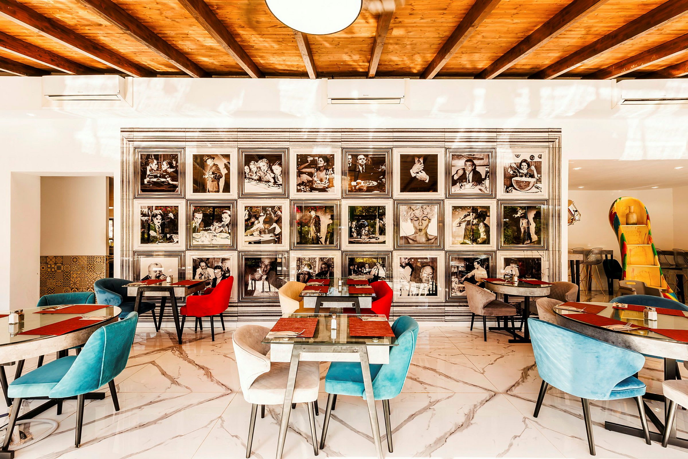 En restaurantinteriør med farvestrålende stole og marmorgulve. På væggen ses sort-hvide fotografier i rammer. (AI-genereret tekst)