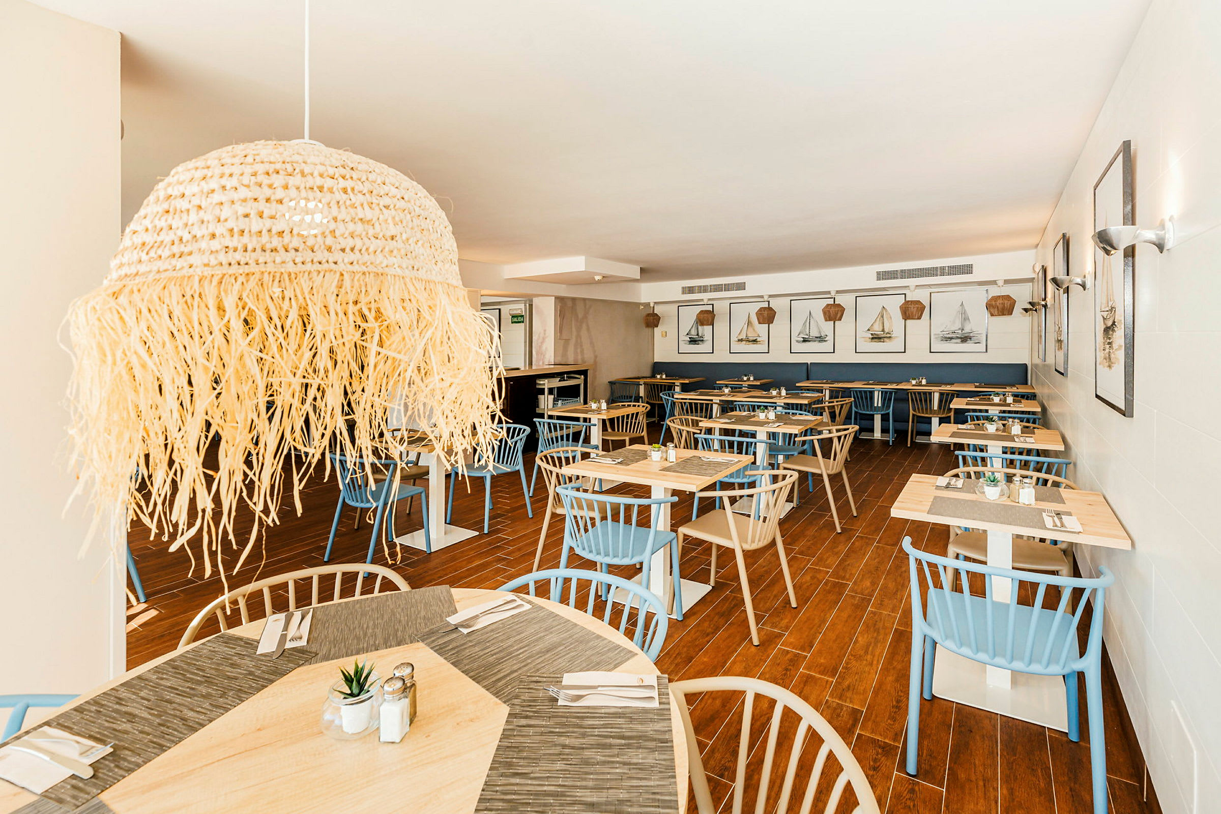 Interiør af en restaurant med træborde, blå og beige stole samt vægdekorationer med bådmotiver. (AI-genereret tekst)
