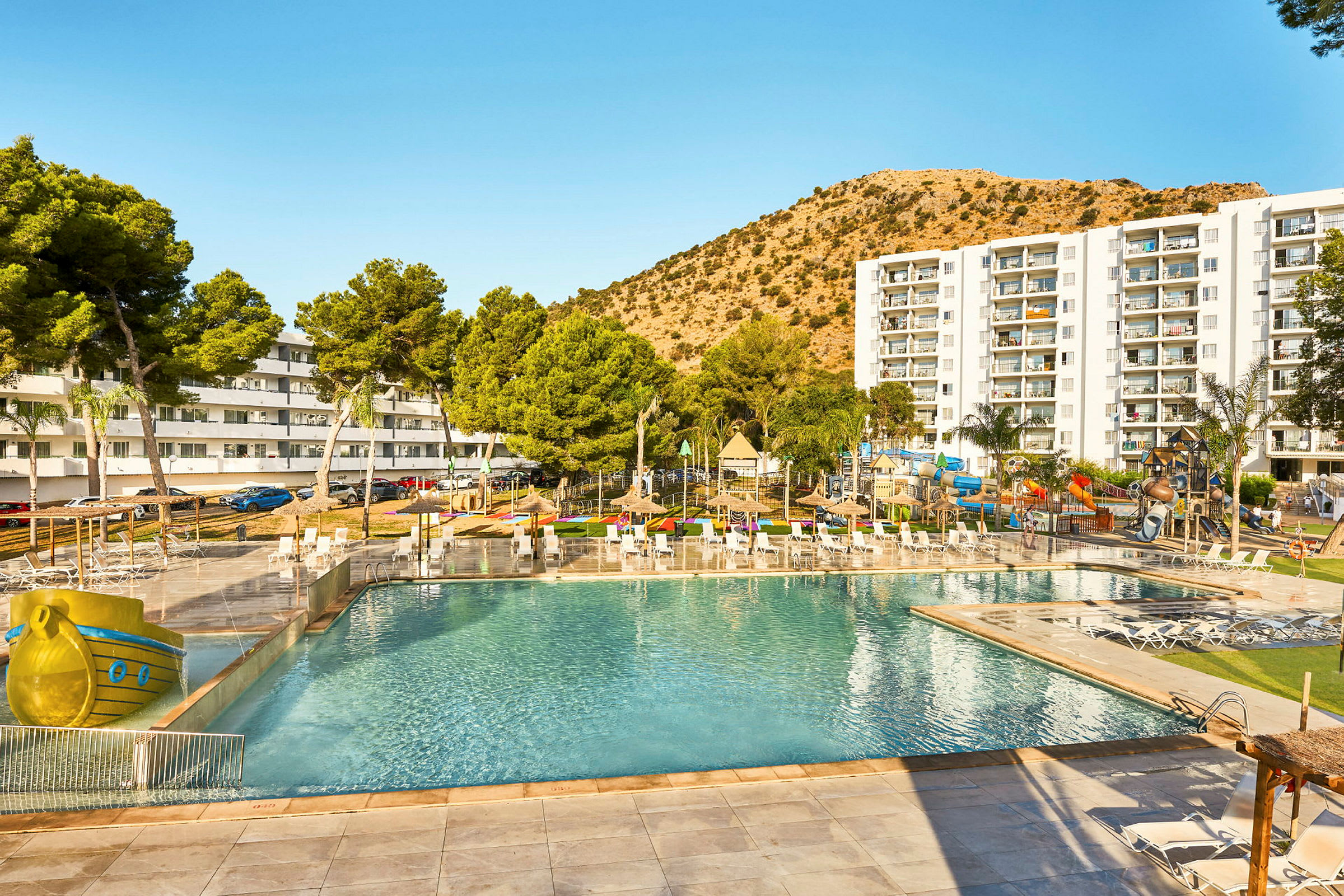 Feriehotel med poolområde, liggestole og en legeplads til børn i en solrig atmosfære. (AI-genereret tekst)