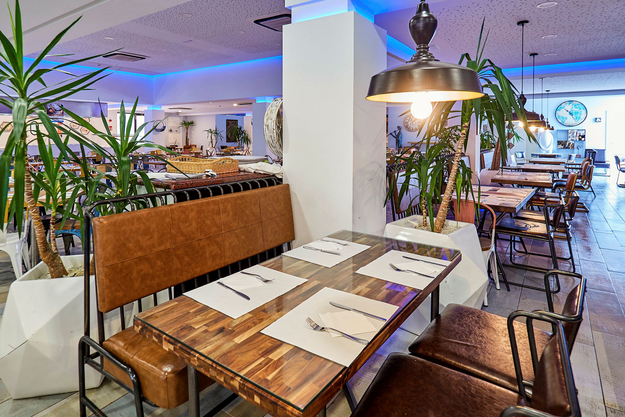 En restaurantindretning med borde og stole, dekoreret med indendørs planter og belysning. (AI-genereret tekst)