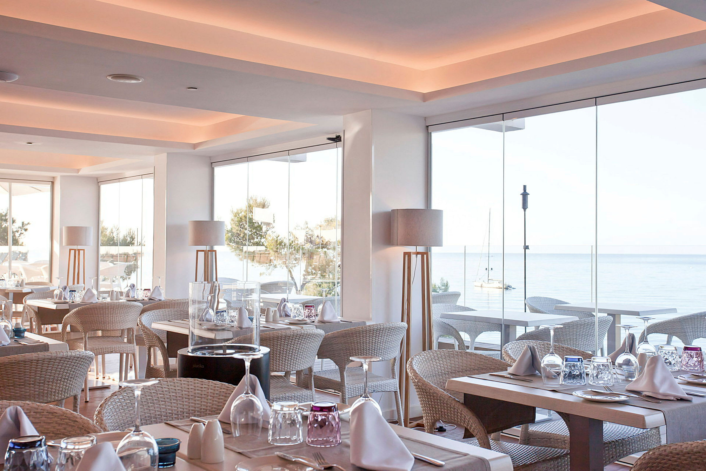 Lyst og moderne indrettet restaurantområde med udsigt over havet gennem store glasvinduer. (AI-genereret tekst)