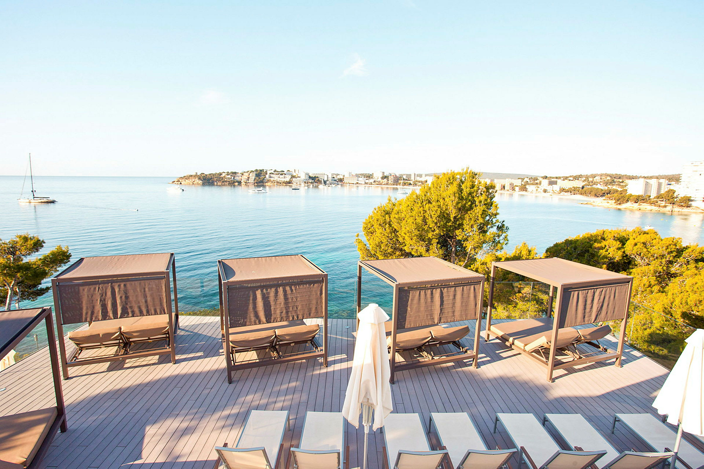 Solsenge og skyggebeskyttelse på en terrasse med udsigt over havet og en bugt. (AI-genereret tekst)