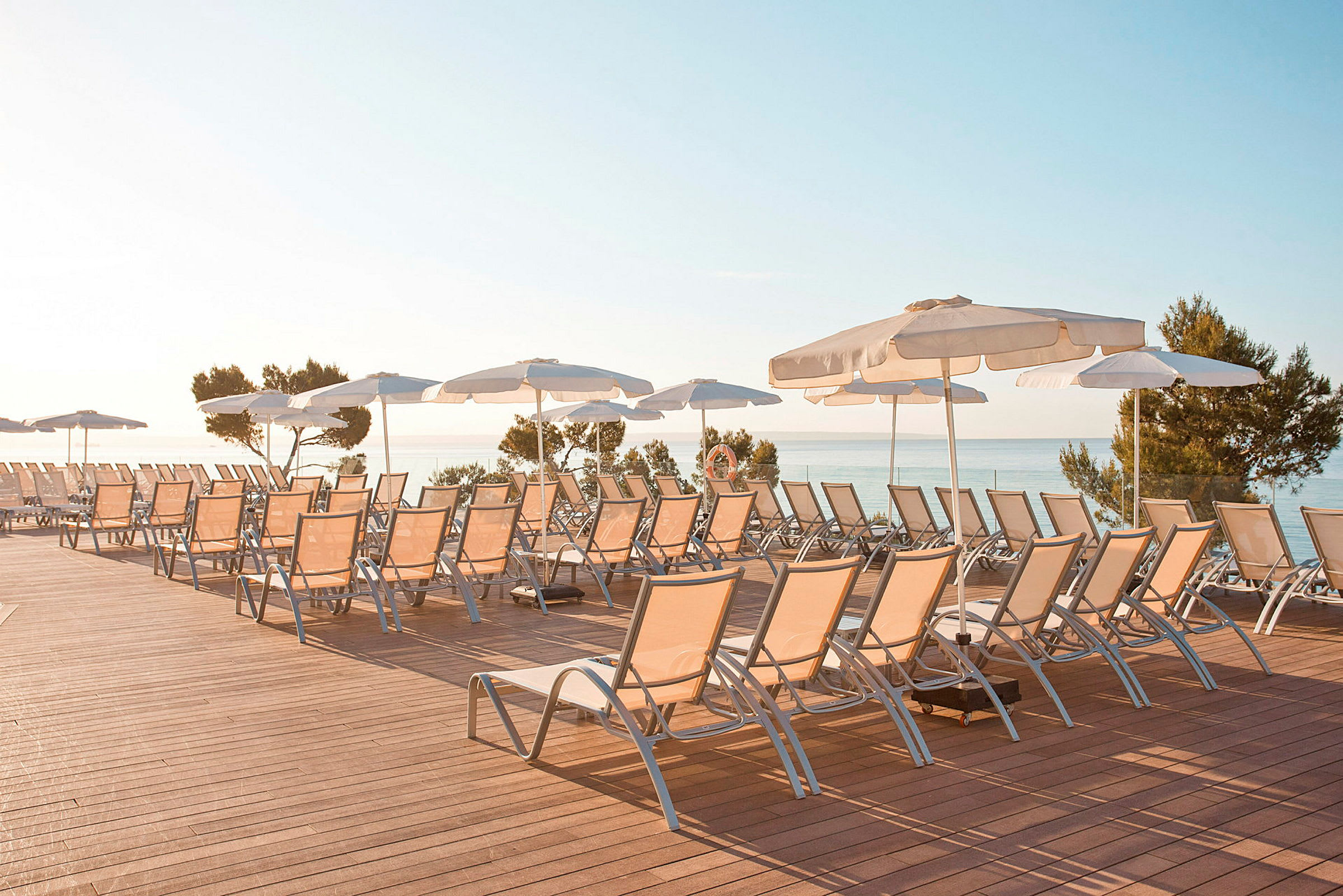 Liggestole og parasoller på en terrasse med udsigt over havet. (AI-genereret tekst)