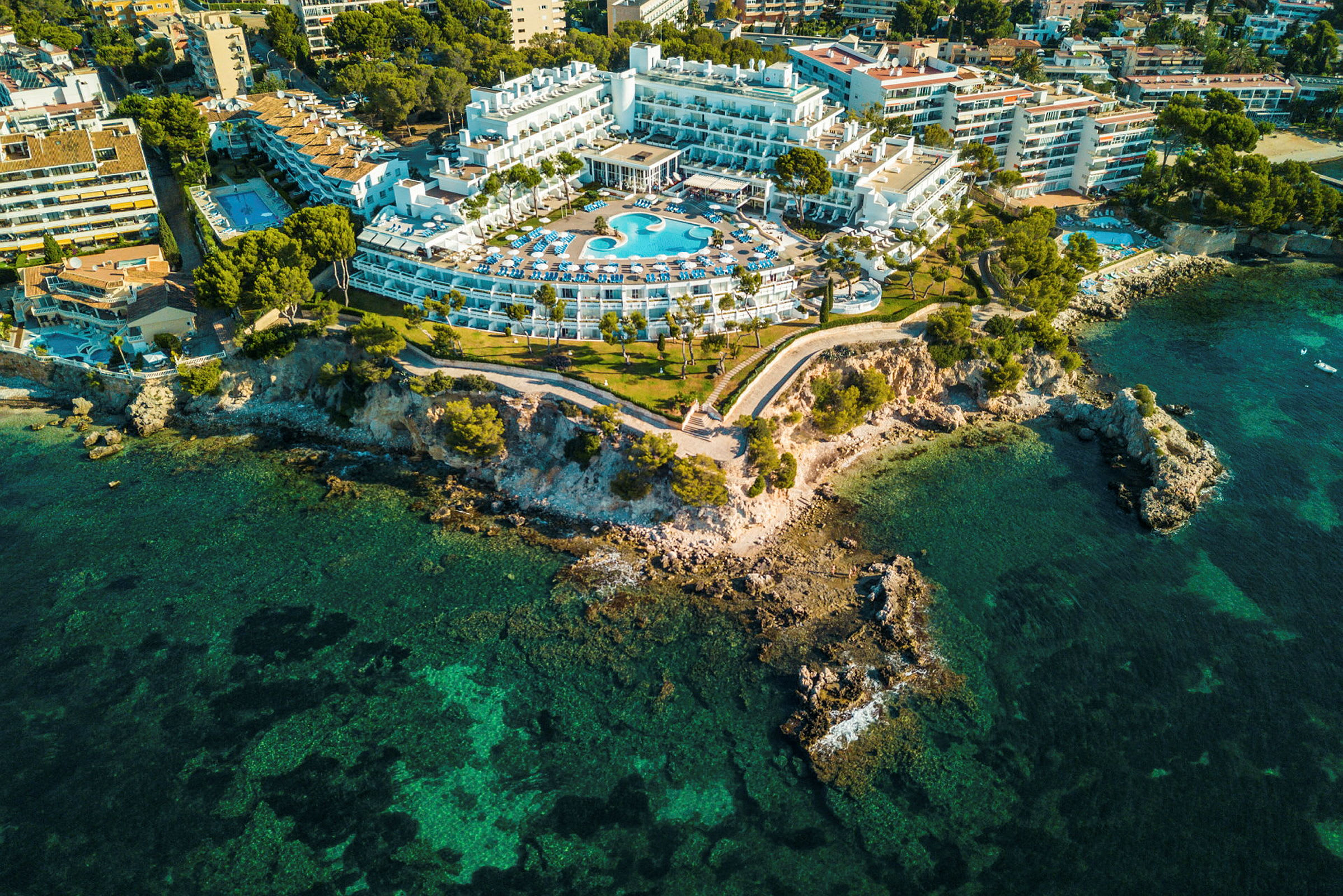 Luftfoto af et hotel med swimmingpool, beliggende ved en klippekyst. (AI-genereret tekst)