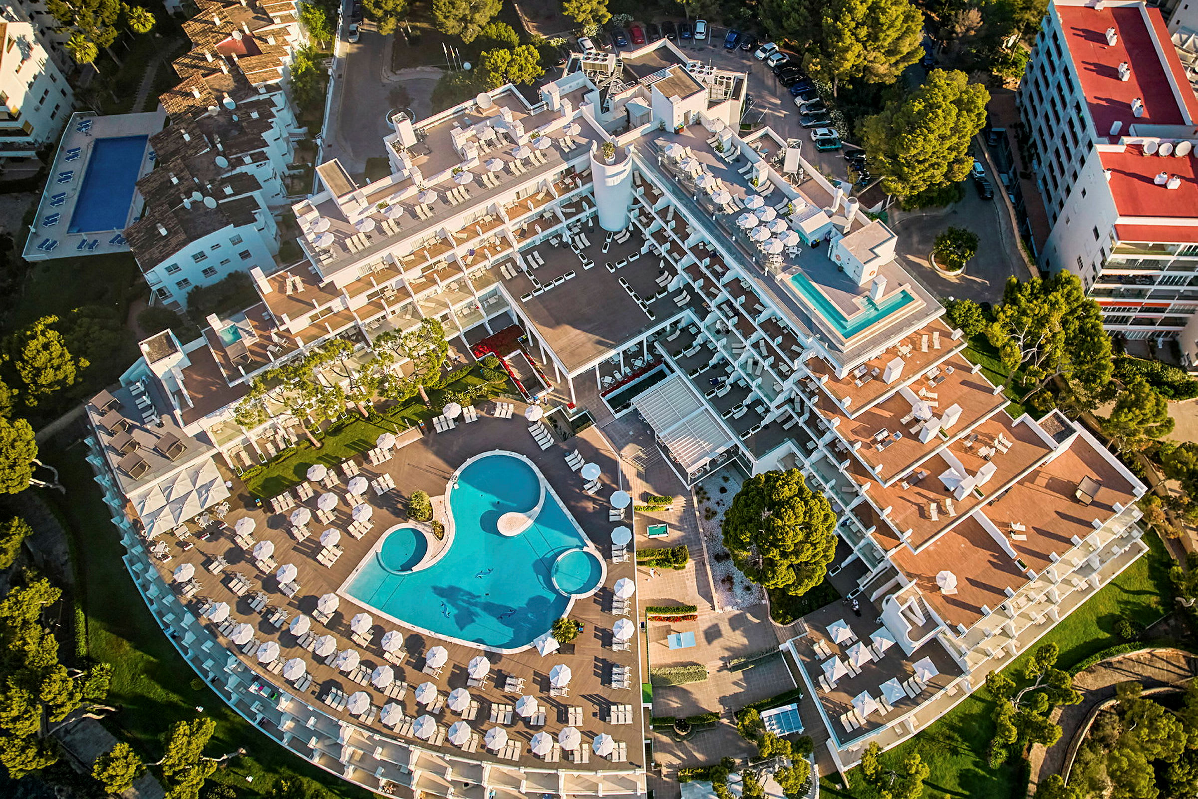 Luftfoto af en hotelbygning med udsigt over et poolområde og solsenge. (AI-genereret tekst)