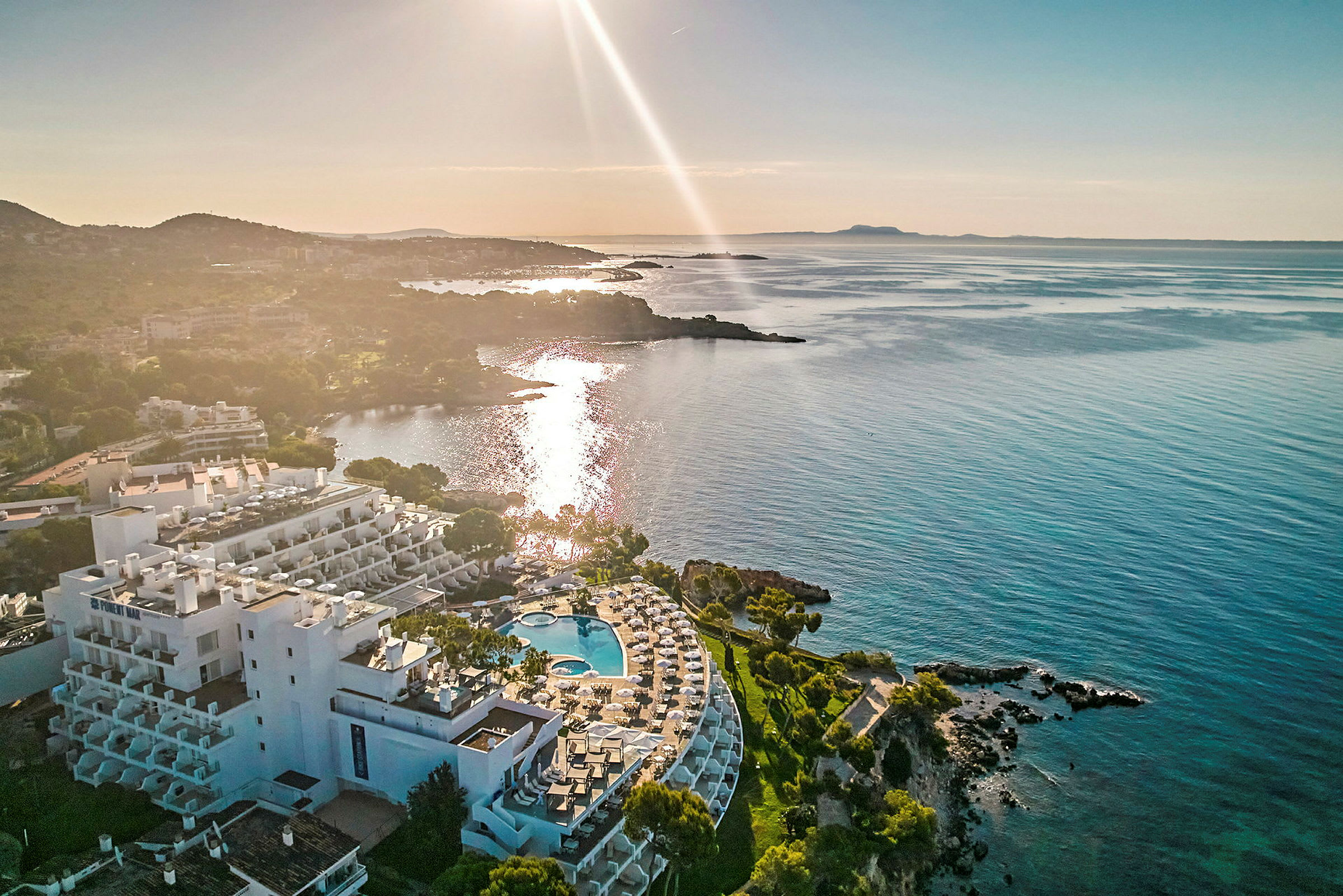 Luftudsigt over et kystnært hotel med poolområde og udsigt over havet ved solnedgang. (AI-genereret tekst)