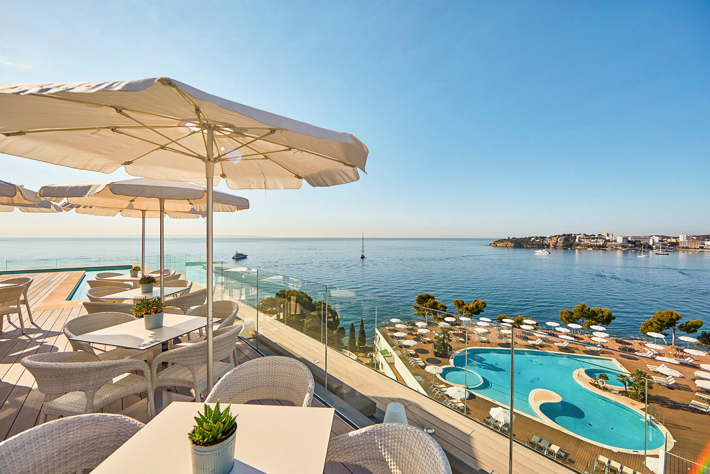 Billede der viser en terrasse med siddepladser og parasoller, med udsigt over en pool og havet. (AI-genereret tekst)