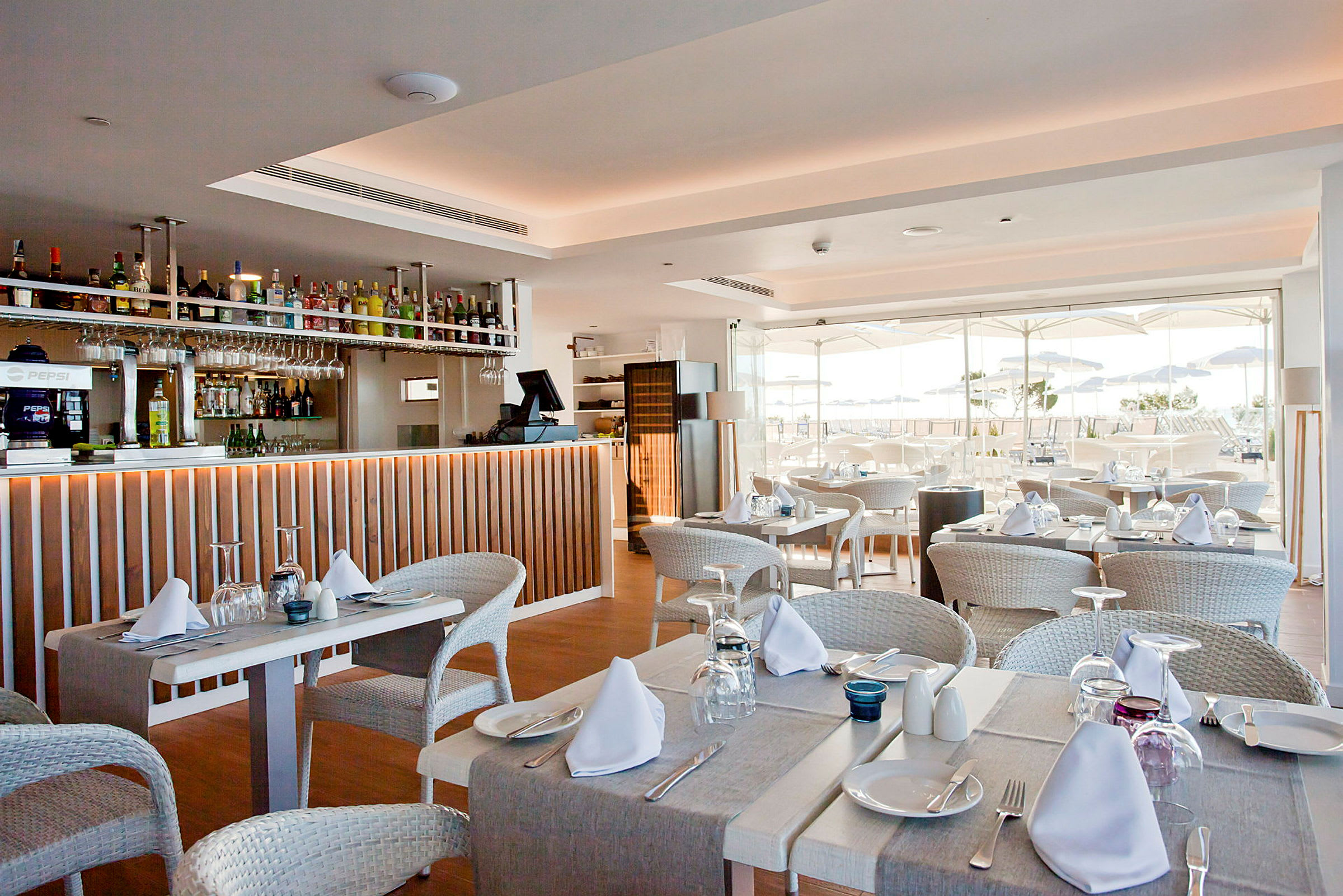 Restaurant med dækkede borde og bar. Udsigt til udendørsterrasse med parasoller. (AI-genereret tekst)