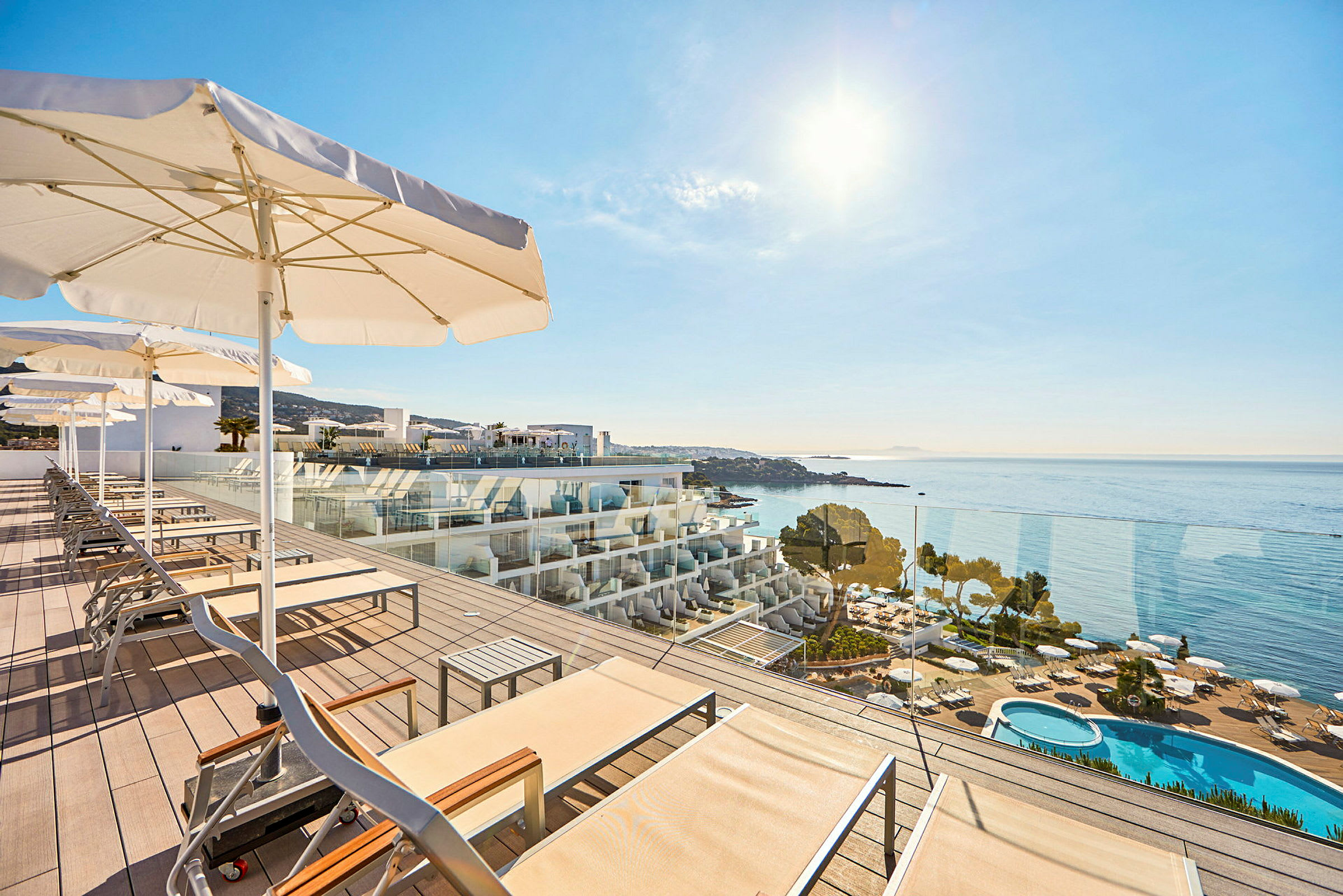 Solstole og parasoller på en terrasse med udsigt over havet og en swimmingpool. (AI-genereret tekst)