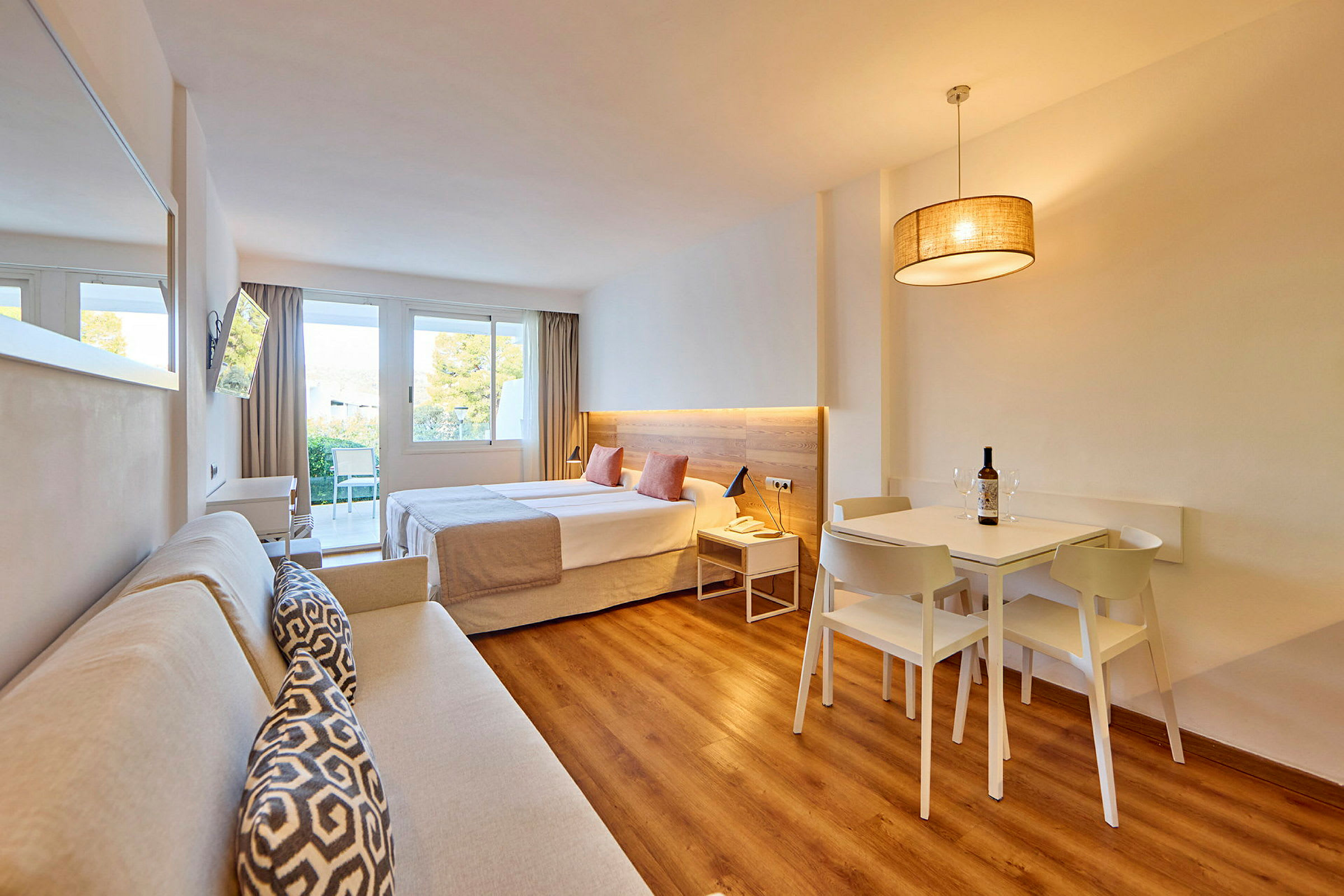 Et moderne hotelværelse med en dobbeltseng, sofa, spisebord og store vinduer, der lukker naturligt lys ind. (AI-genereret tekst)