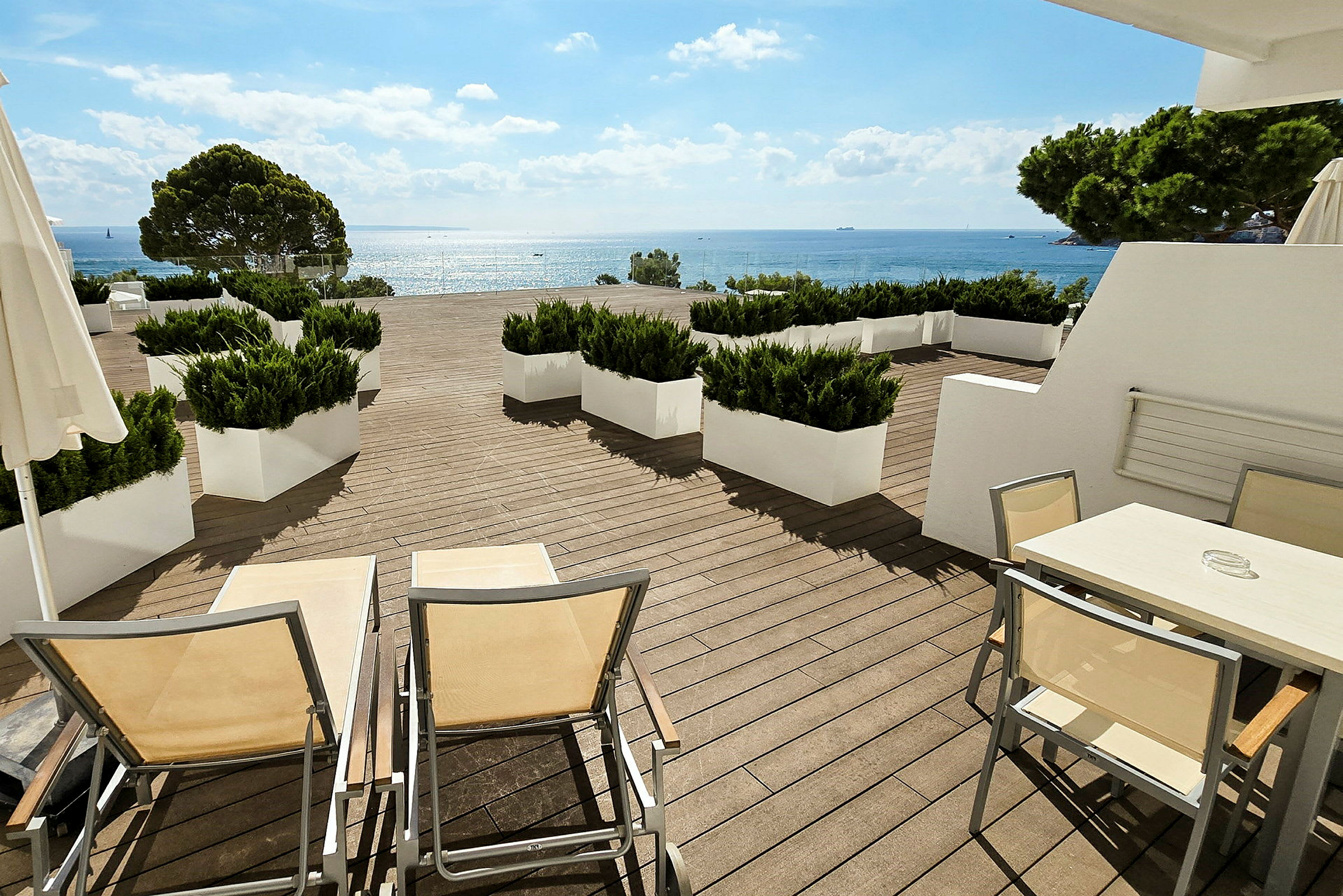 Terrasse med udsigt over havet, dekoreret med hvide møbler og plantebegrænsninger. (AI-genereret tekst)