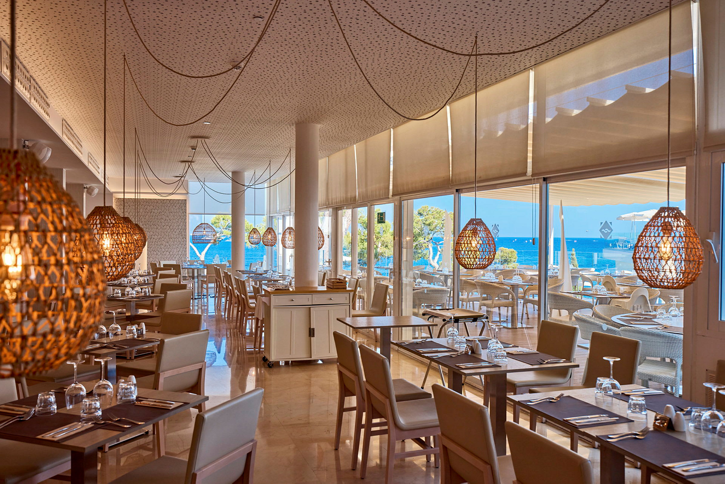 Restaurant med borde og stole, store vinduer med udsigt til havet. (AI-genereret tekst)