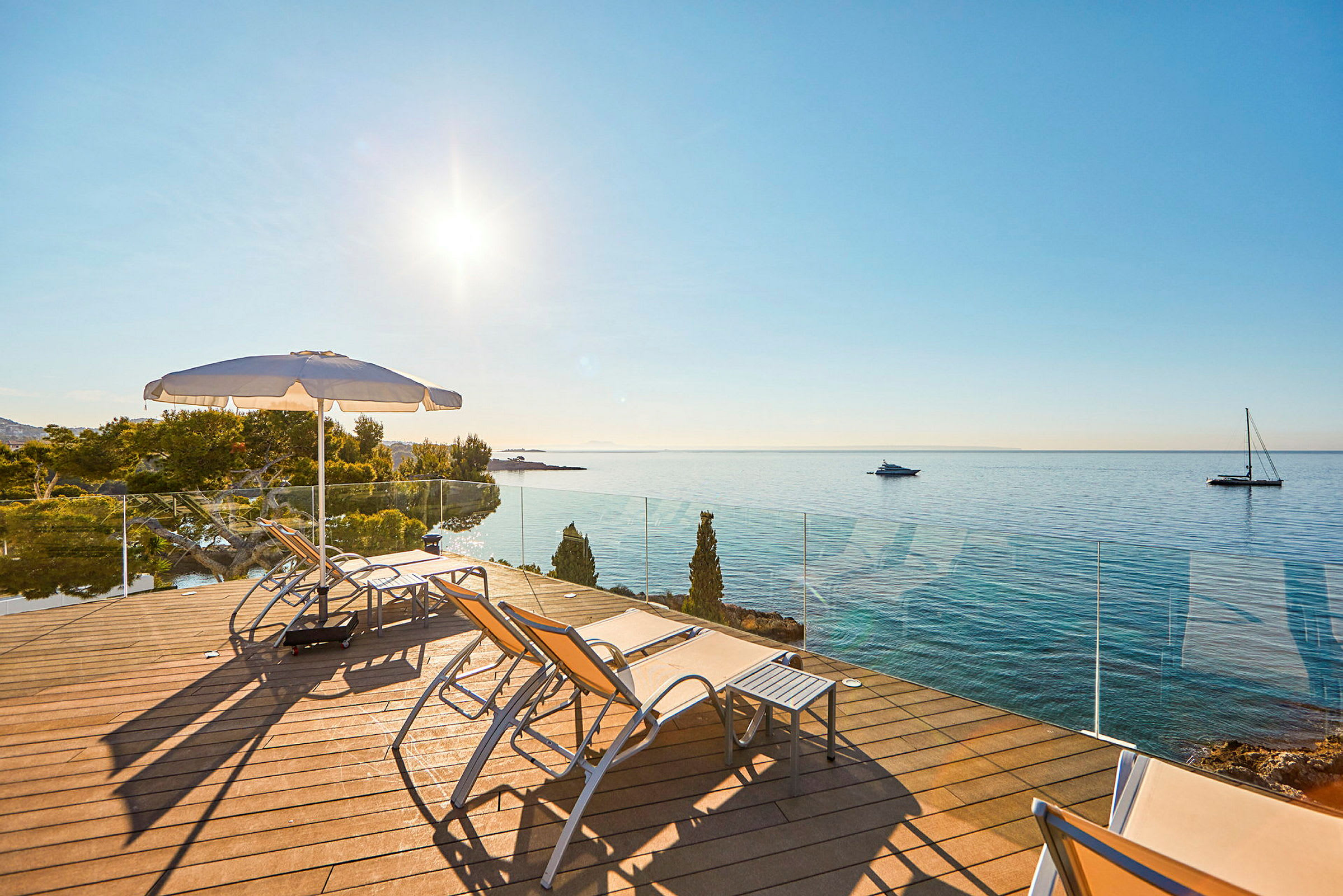 Liggestole og parasol på en terrasse med udsigt over havet. (AI-genereret tekst)