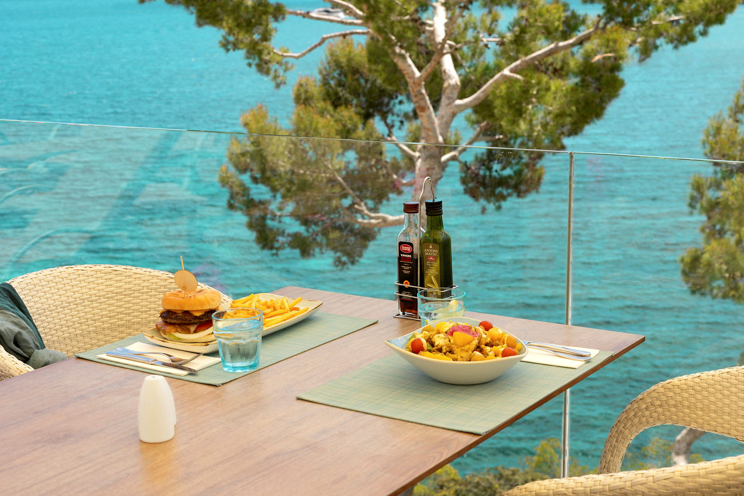 En terrasse med udsigt over havet, hvor et bord er dækket med en burger, pommes frites og en salat. (AI-genereret tekst)