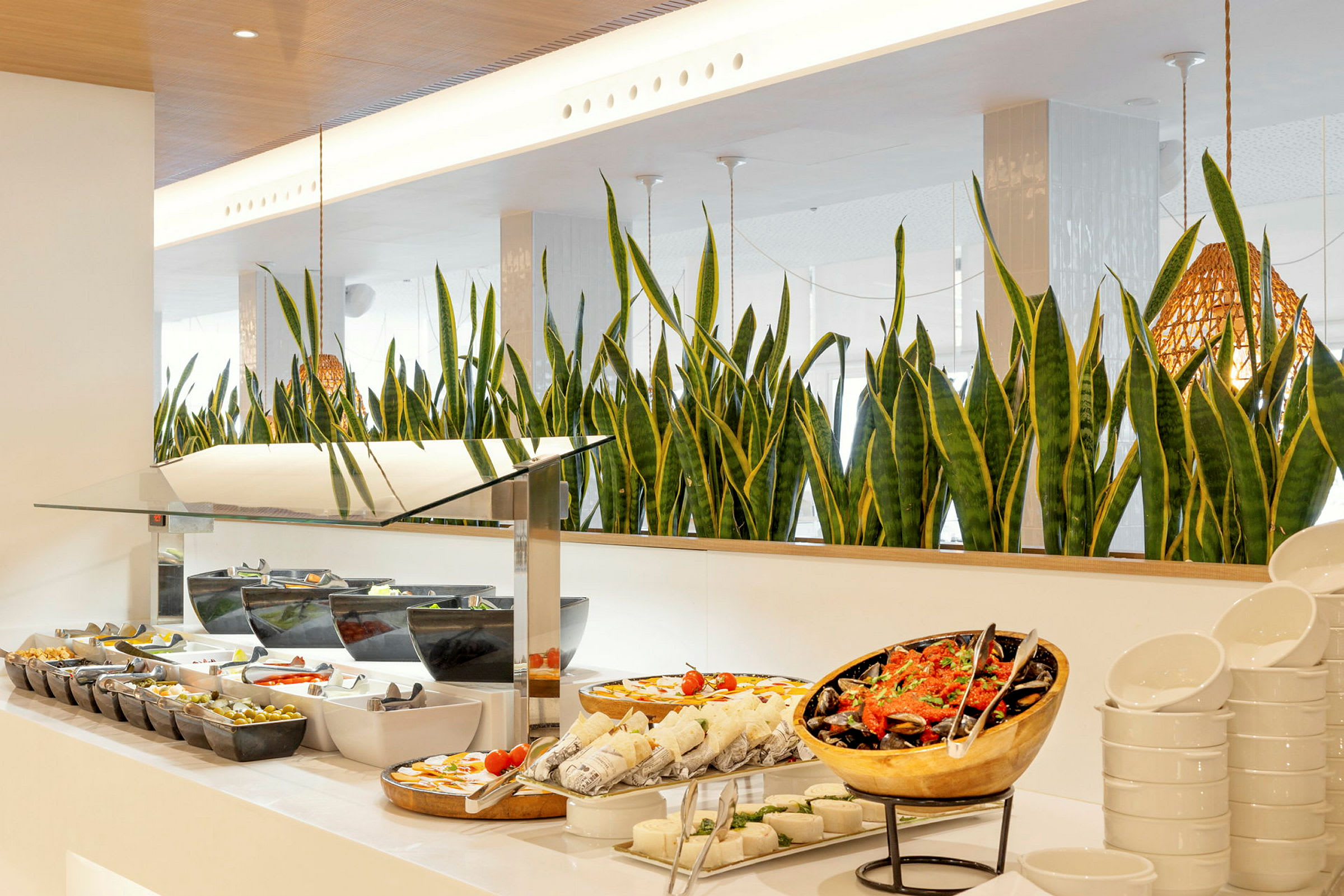 En buffet med forskellige retter, herunder salater og frokostmuligheder, med grønne planter i baggrunden. (AI-genereret tekst)