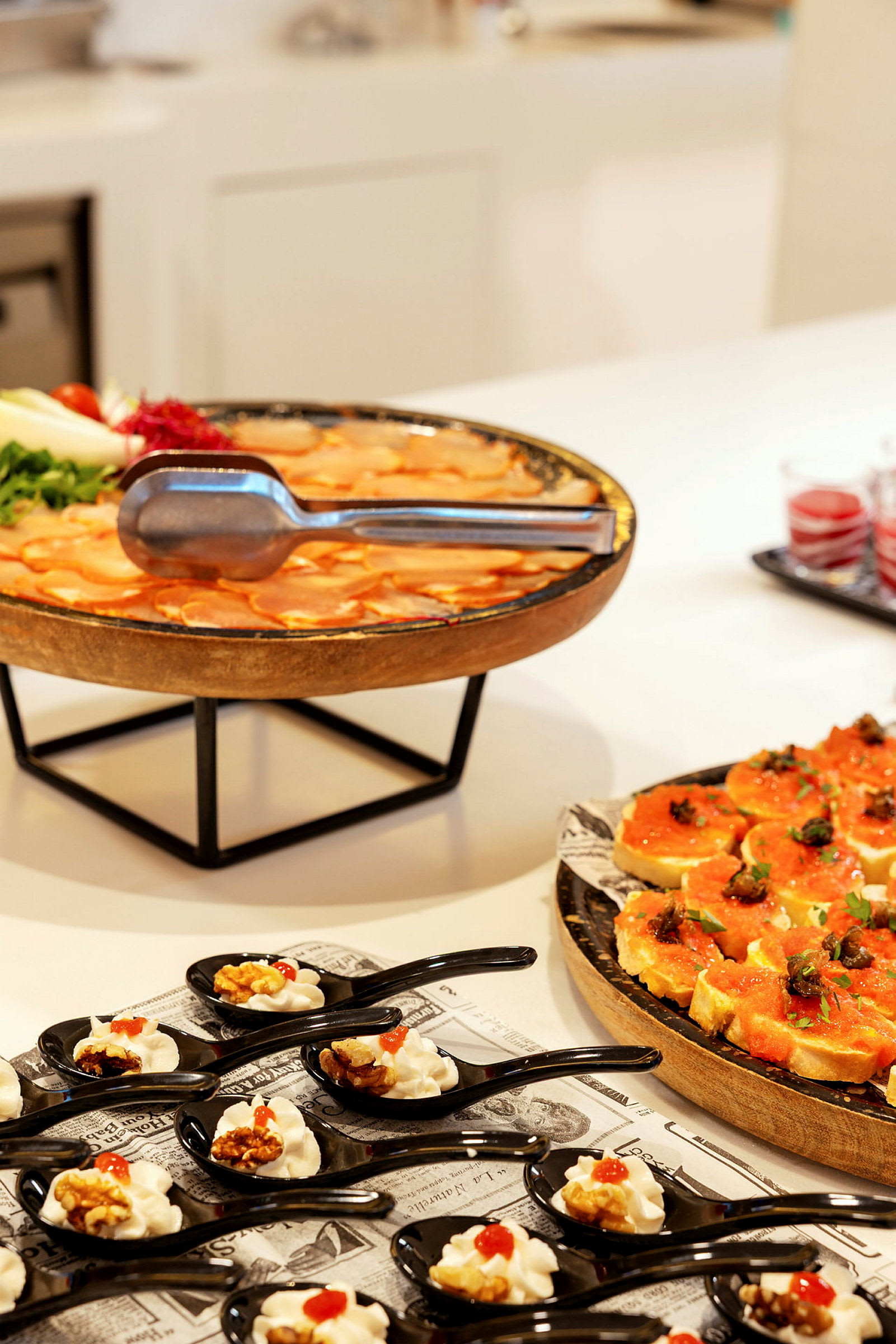 En buffet med forskellige retter, herunder små portioner serveret i sorte skeer, en tallerken med orangefarvet mad og dekorerede brødstykker. (AI-genereret tekst)