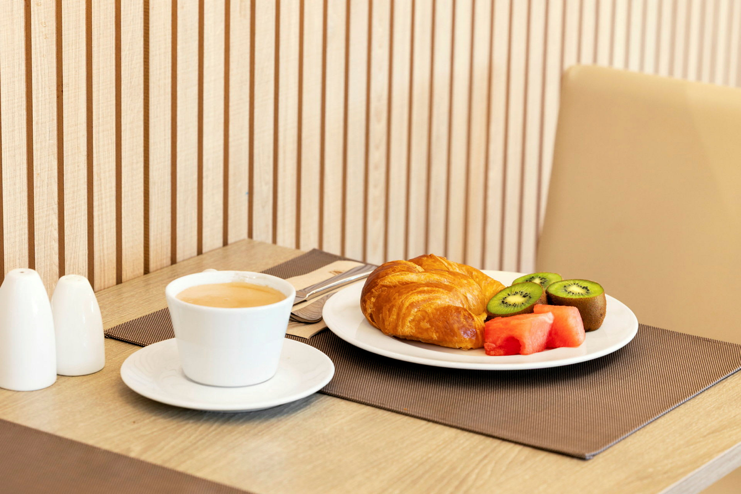 En morgenmad med kaffe, croissant og frisk frugt serveret på bordet. (AI-genereret tekst)
