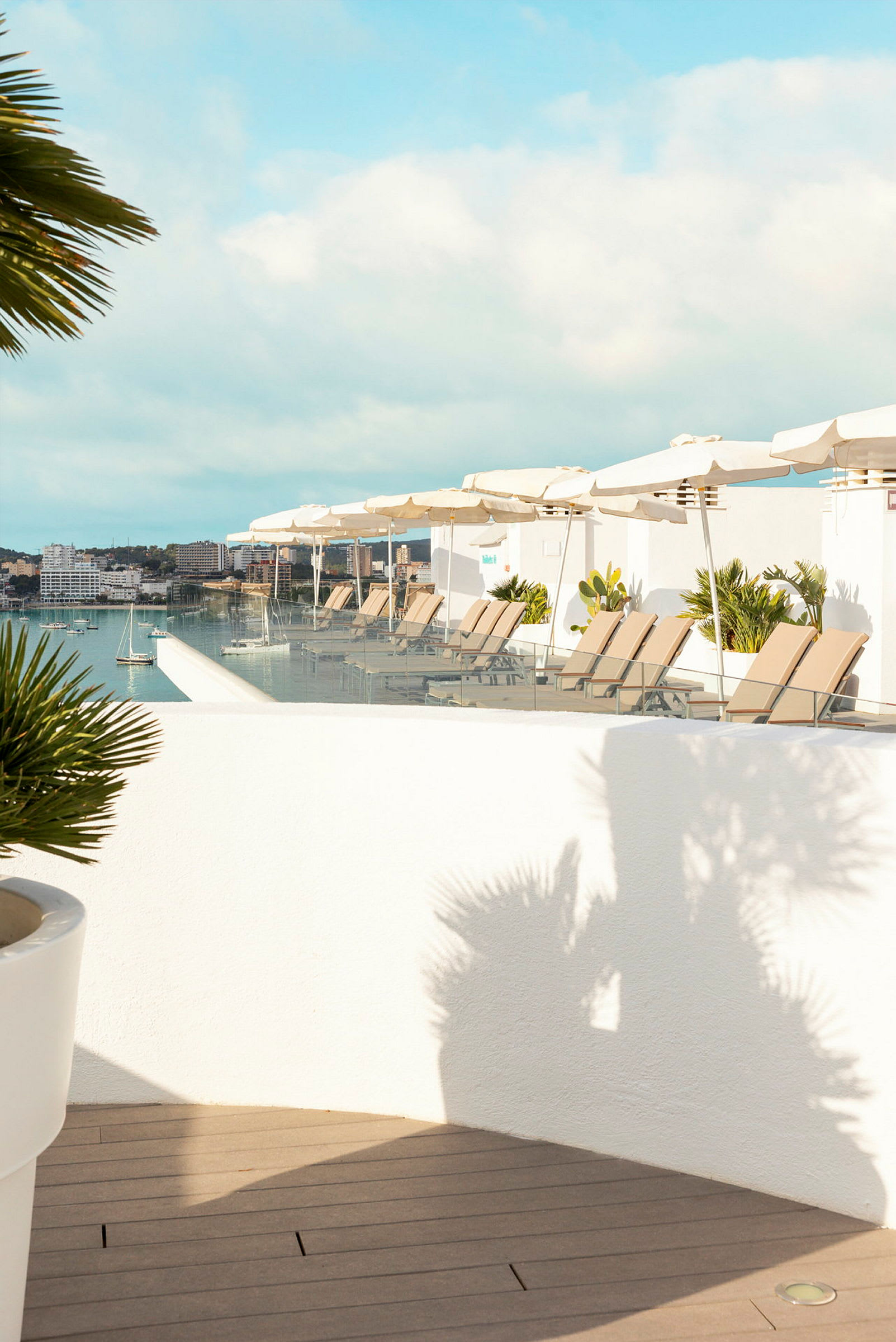 En terrasse med liggestole og parasoller ved en infinitypool med udsigt over en havn. (AI-genereret tekst)