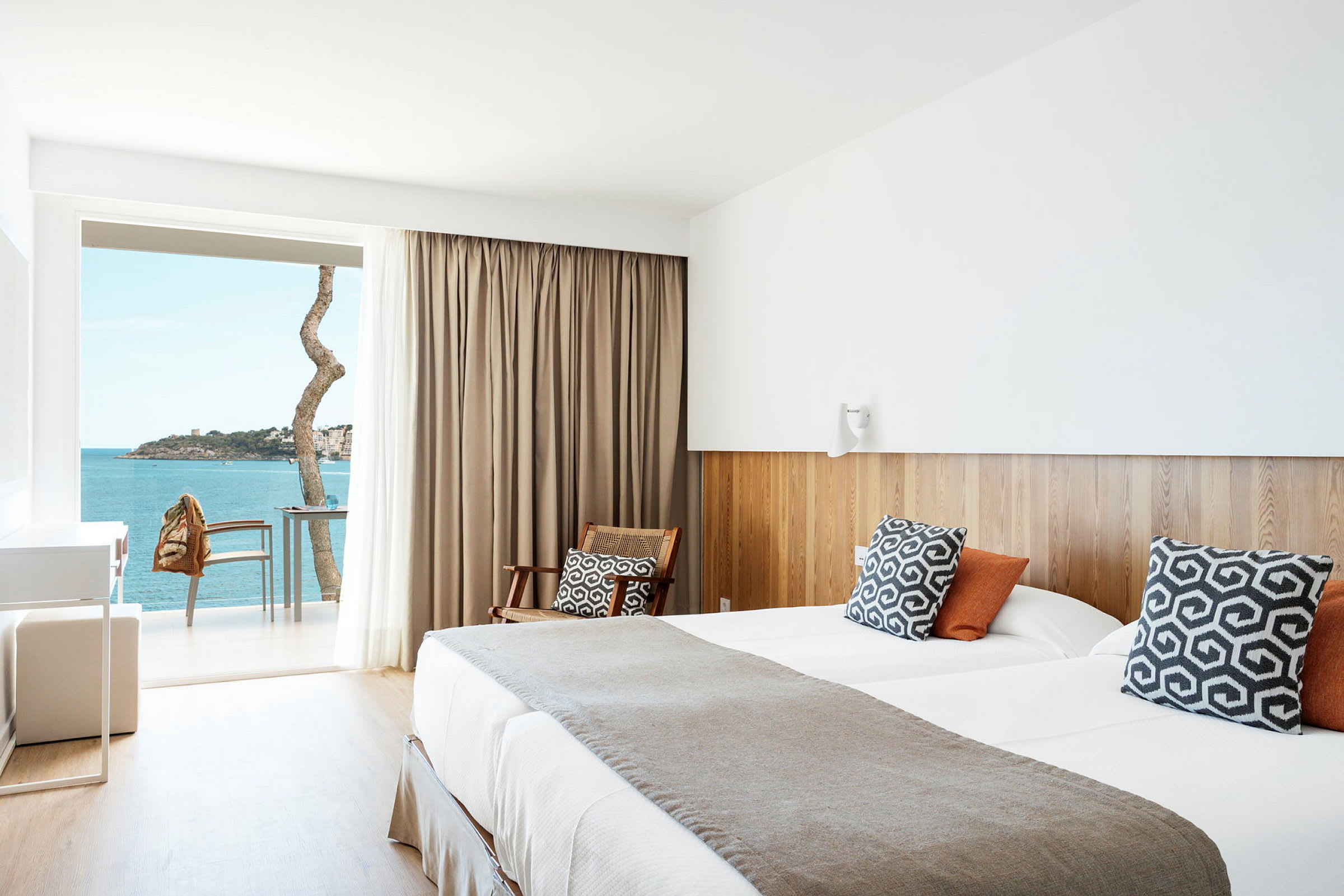 Et hotelværelse med moderne detaljer, en dobbeltseng, rustikke puder, et siddeområde og en balkon med udsigt over havet. (AI-genereret tekst)