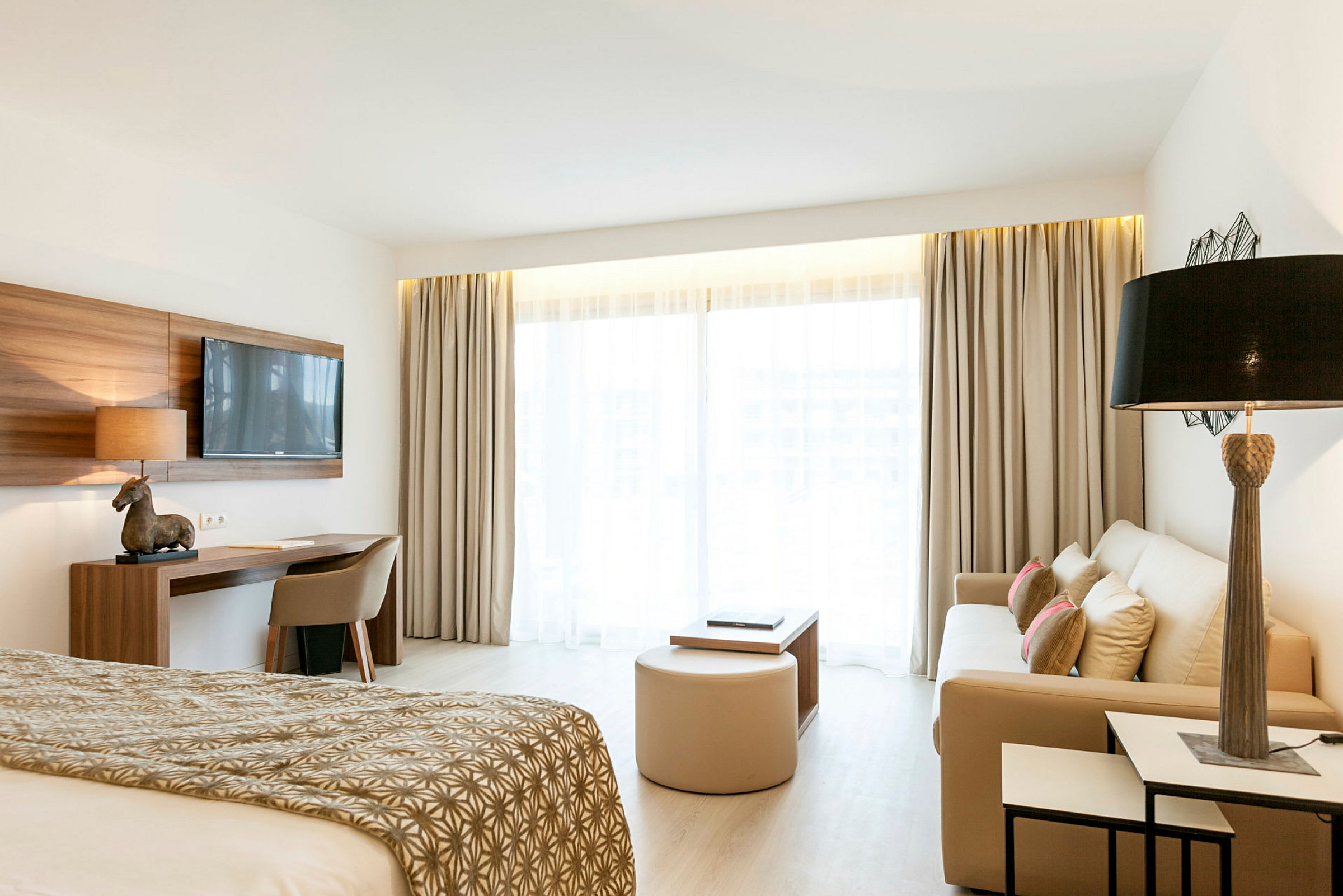 Billede af et lyst hotelværelse med seng, sofa og skrivebord. (AI-genereret tekst)
