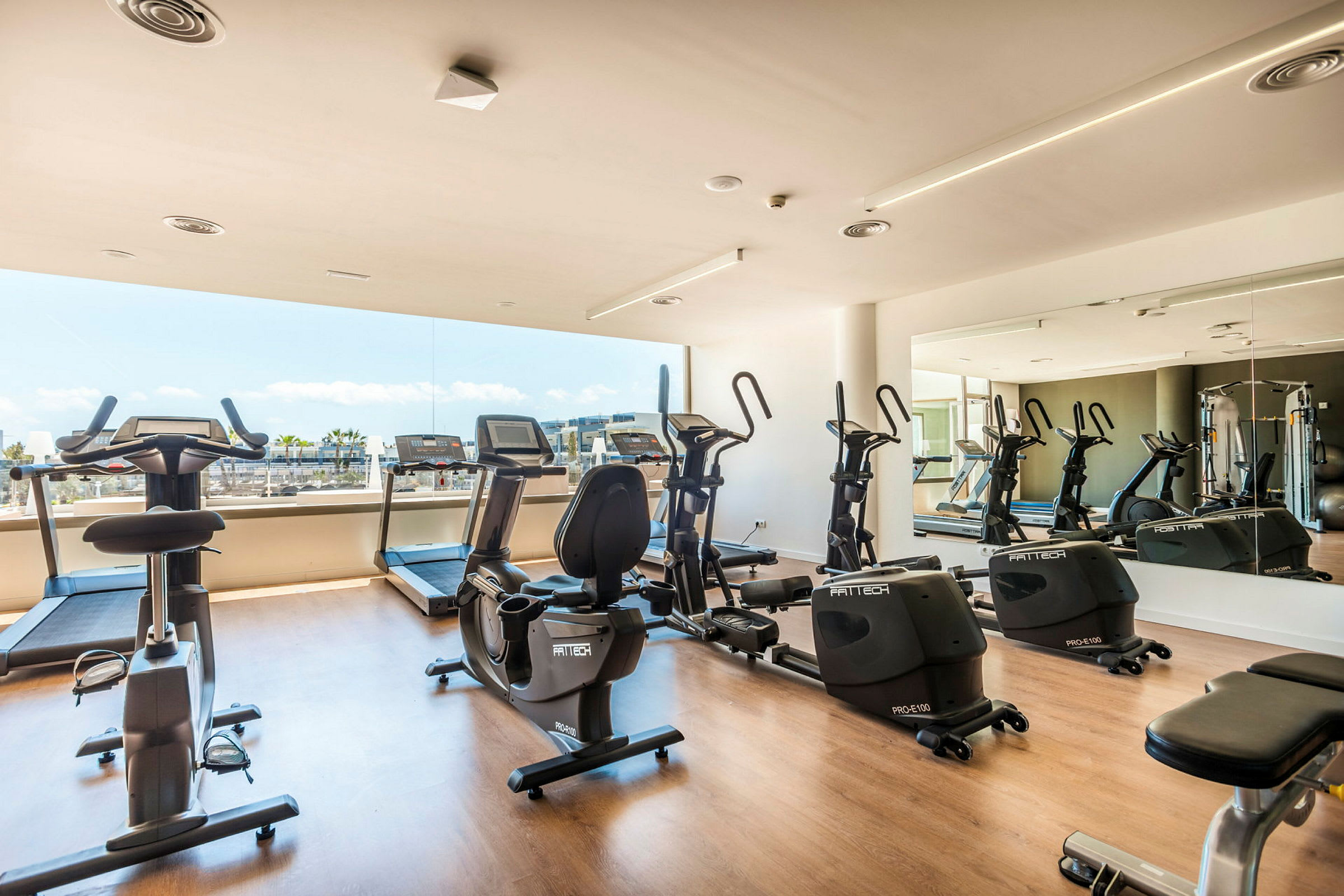 Et fitnesscenter med træningsmaskiner ved en stor vinduesrude. (AI-genereret tekst)